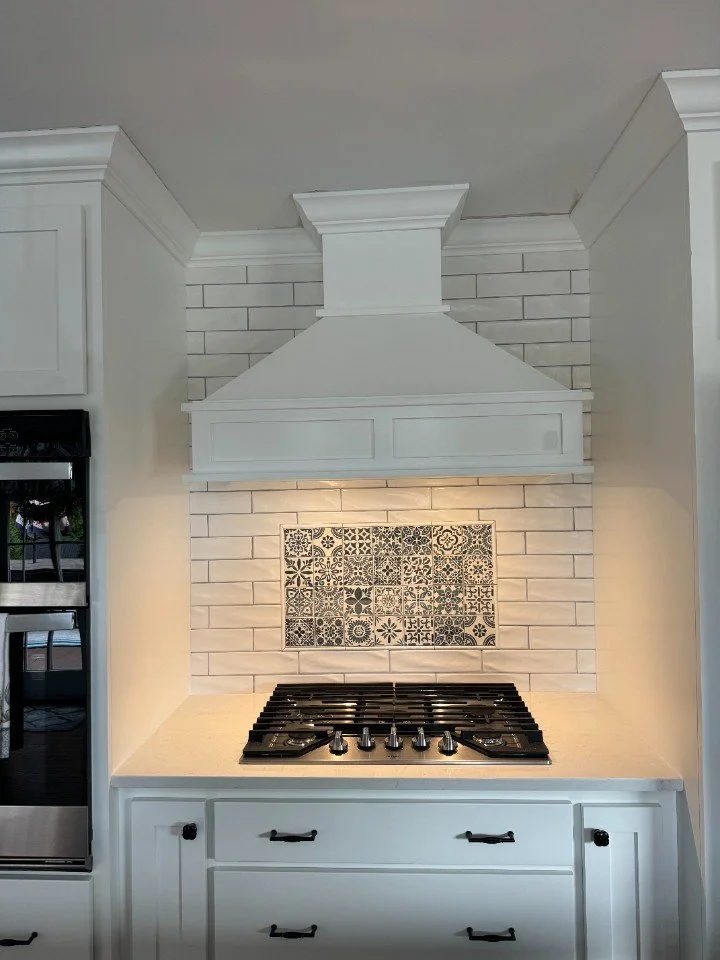 White kitchen range hood above a stovetop with patterned tiles on the backsplash