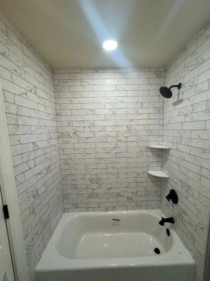 Bathroom shower with white marble tiles, black showerhead, black faucet, and built-in corner shelves.