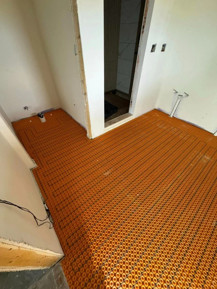 Room under construction with orange underfloor heating mats, unfinished drywall, and electrical outlets without cover plates.