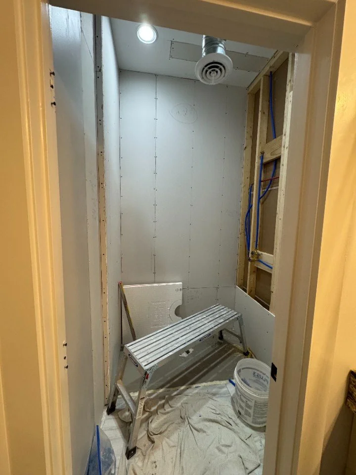 A small bathroom under construction with unfinished walls, a stepladder, a bucket, and construction materials.