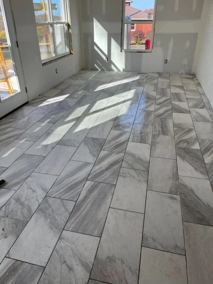 Empty room with large windows letting in sunlight, partially finished walls, and a marble tile floor.