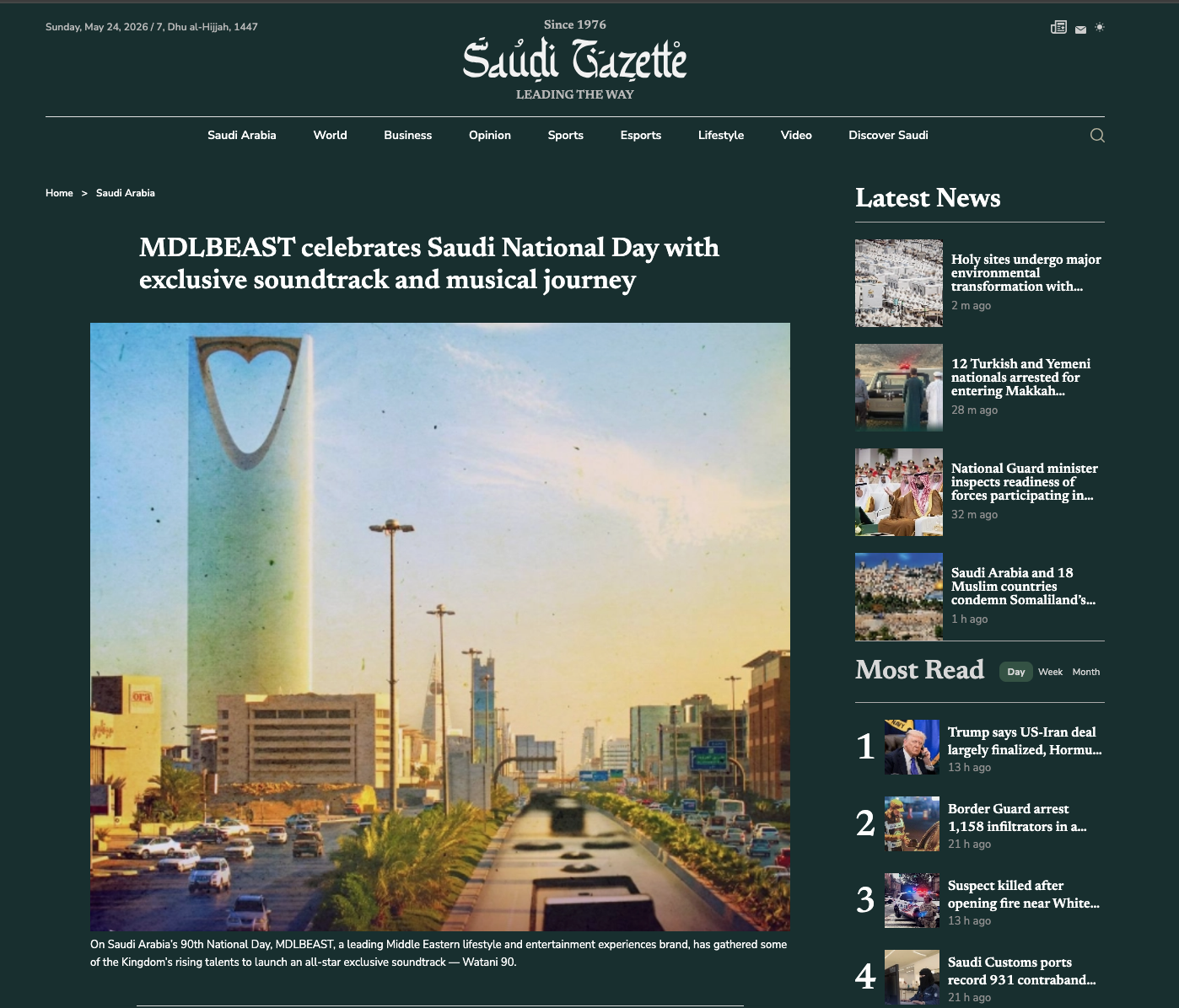 Screenshot of Saudi Gazette news website with headline about celebrating Saudi National Day, showing a cityscape with tall buildings and the Kingdom Tower with the heart-shaped top, under a sky with some clouds.