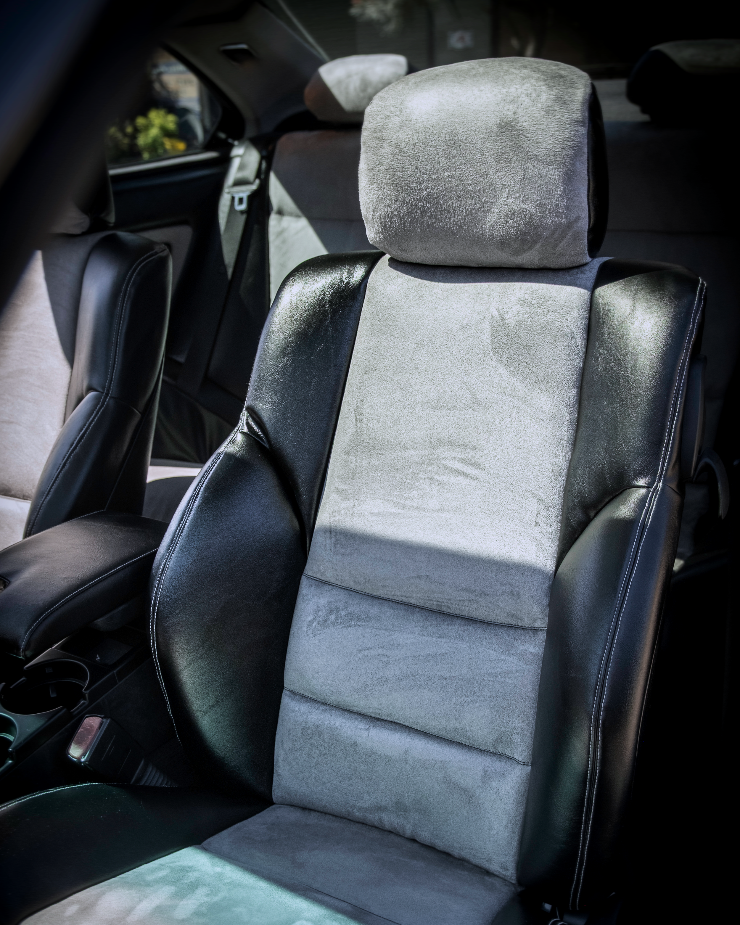 Close-up detailed view of premium custom car seat upholstery by Visions Customs Castle Hill. High-end automotive retrim featuring black vinyl bolsters, white contrast stitching, and a tailored grey suede center insert with a matching headrest.