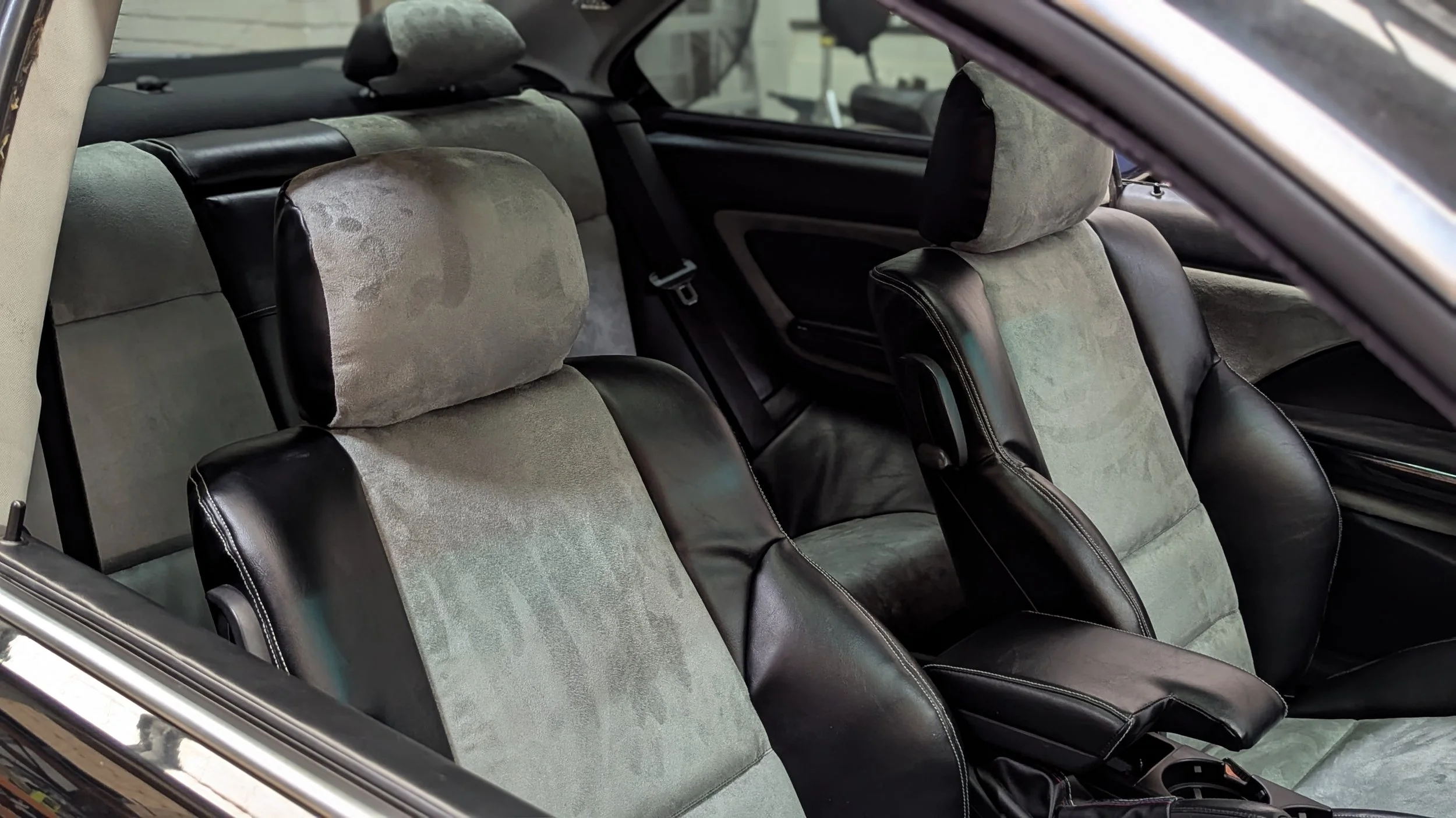 Premium custom car seat retrim by Visions Customs in the Hills District. Detailed view of a complete auto interior restoration, highlighting black vinyl bolsters, grey suede center inserts, and matching two-tone headrests on front and rear seats.