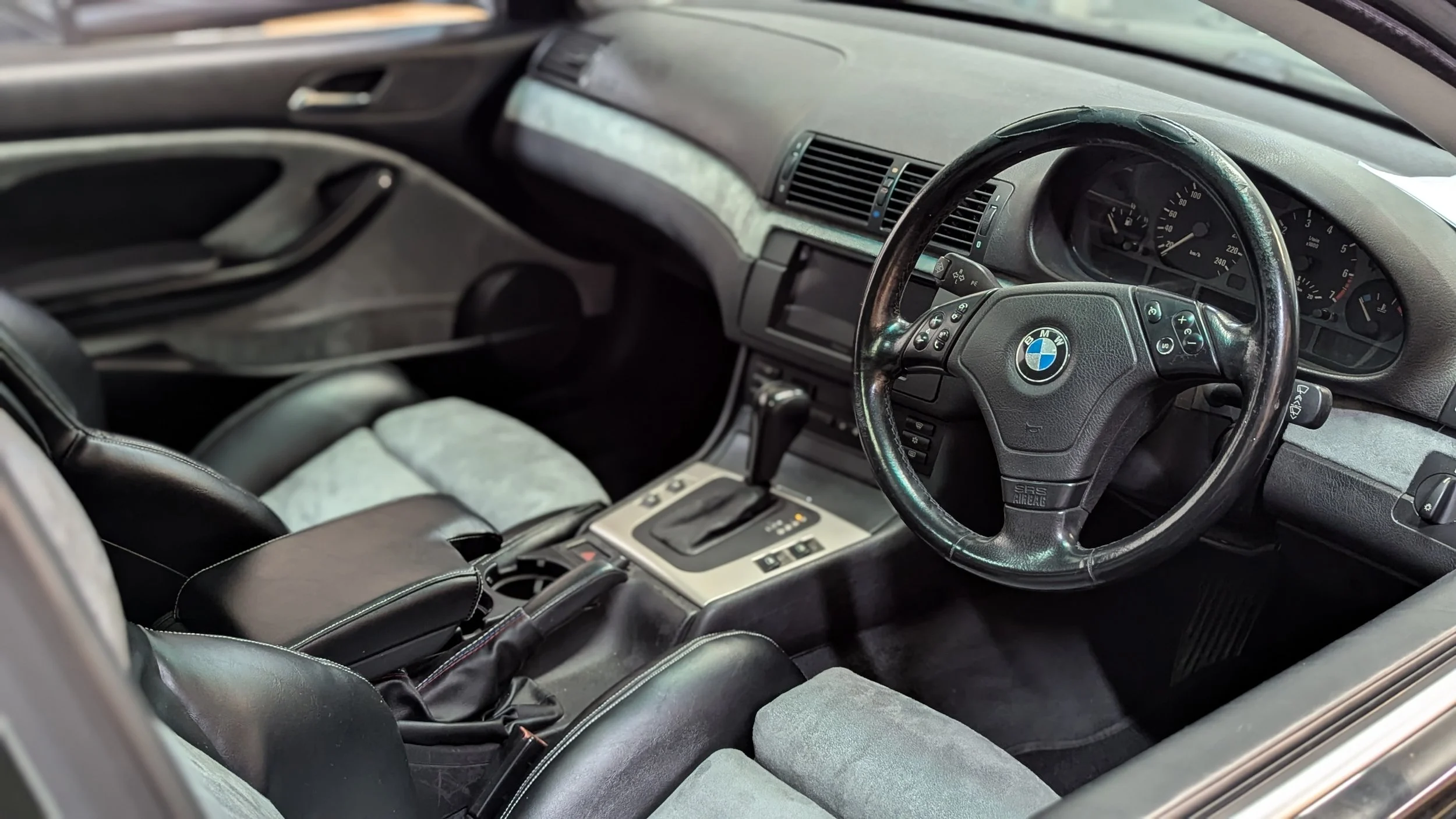 Bespoke BMW interior upholstery by Visions Customs in Castle Hill. Complete high-end cabin restoration featuring black leather and grey suede seats, matching door cards, and custom-requested grey suede dashboard inserts.