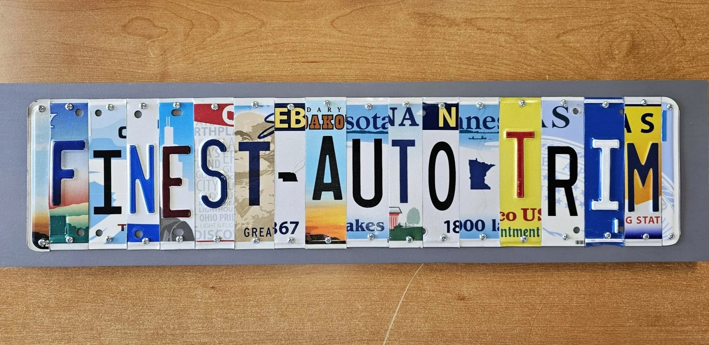 A collage art piece of a license plate displaying the phrase 'FINEST AUTO TEAM' in capital letters.