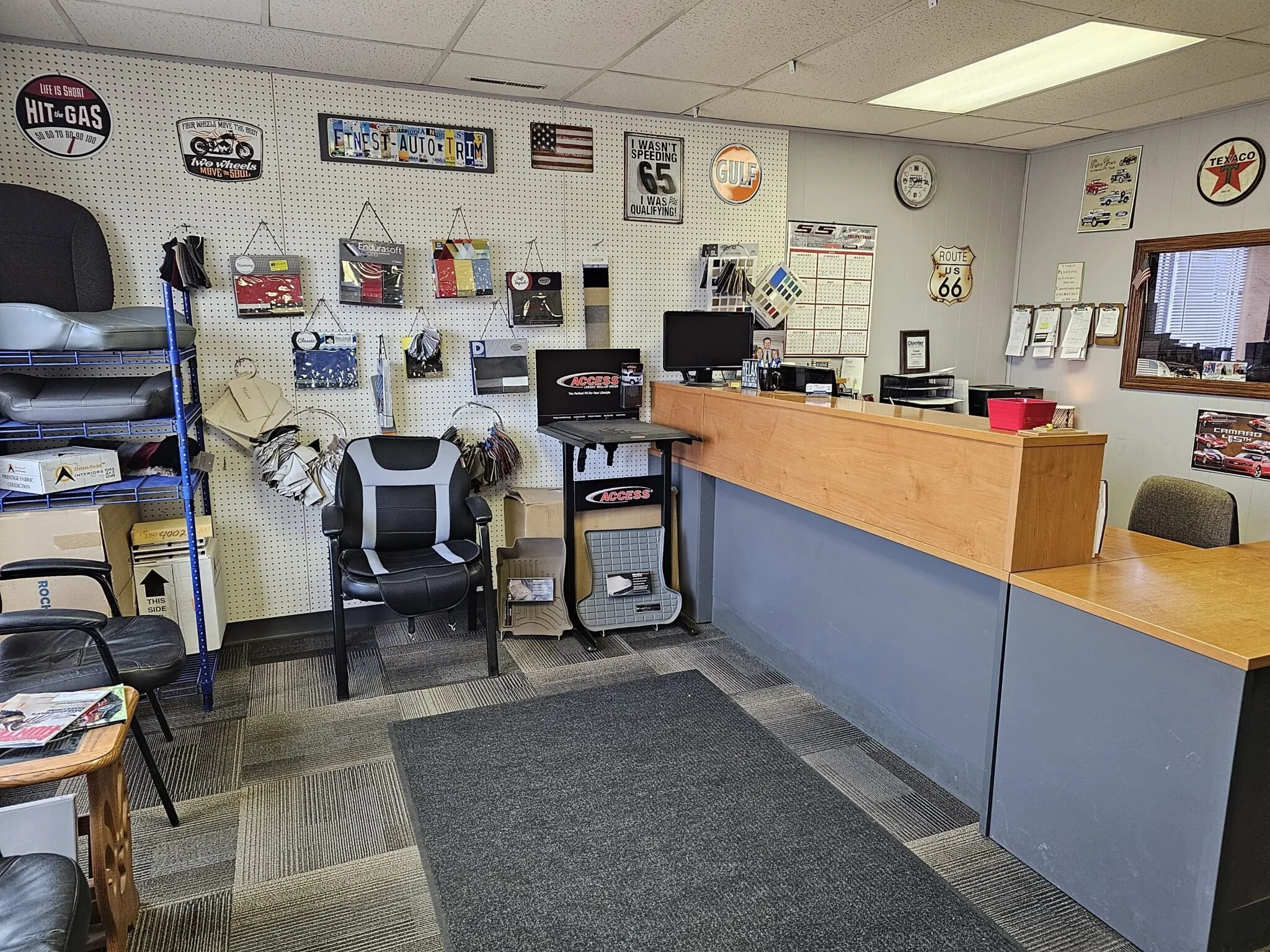 Interior of a Finest Auto Trim, Inc with various automotive-themed signs and decor on the wall, a counter, chairs, and shelves with car accessories and samples.