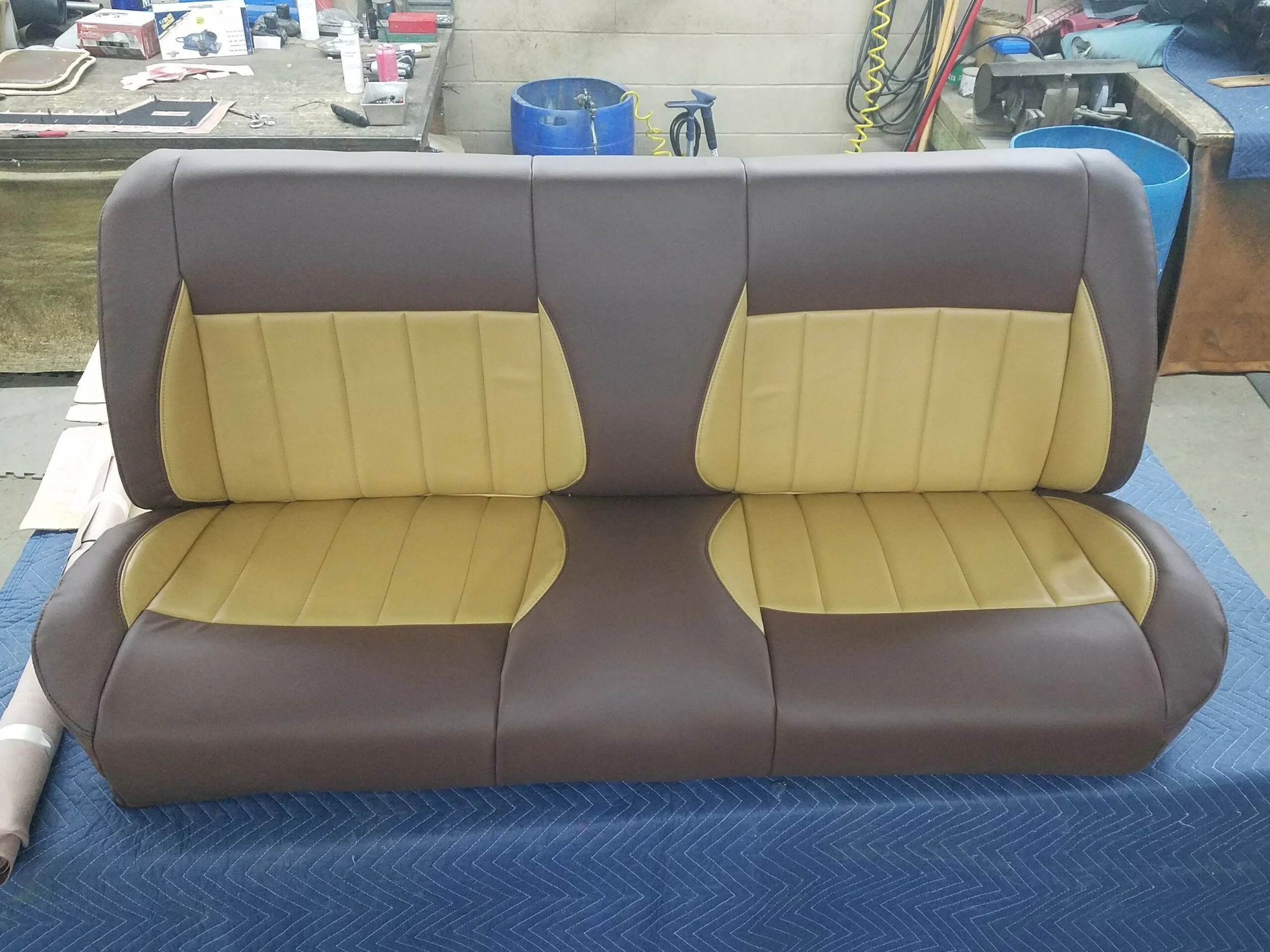 A vintage truck bench seat with a two-tone tan and brown upholstery, built up bolsters.