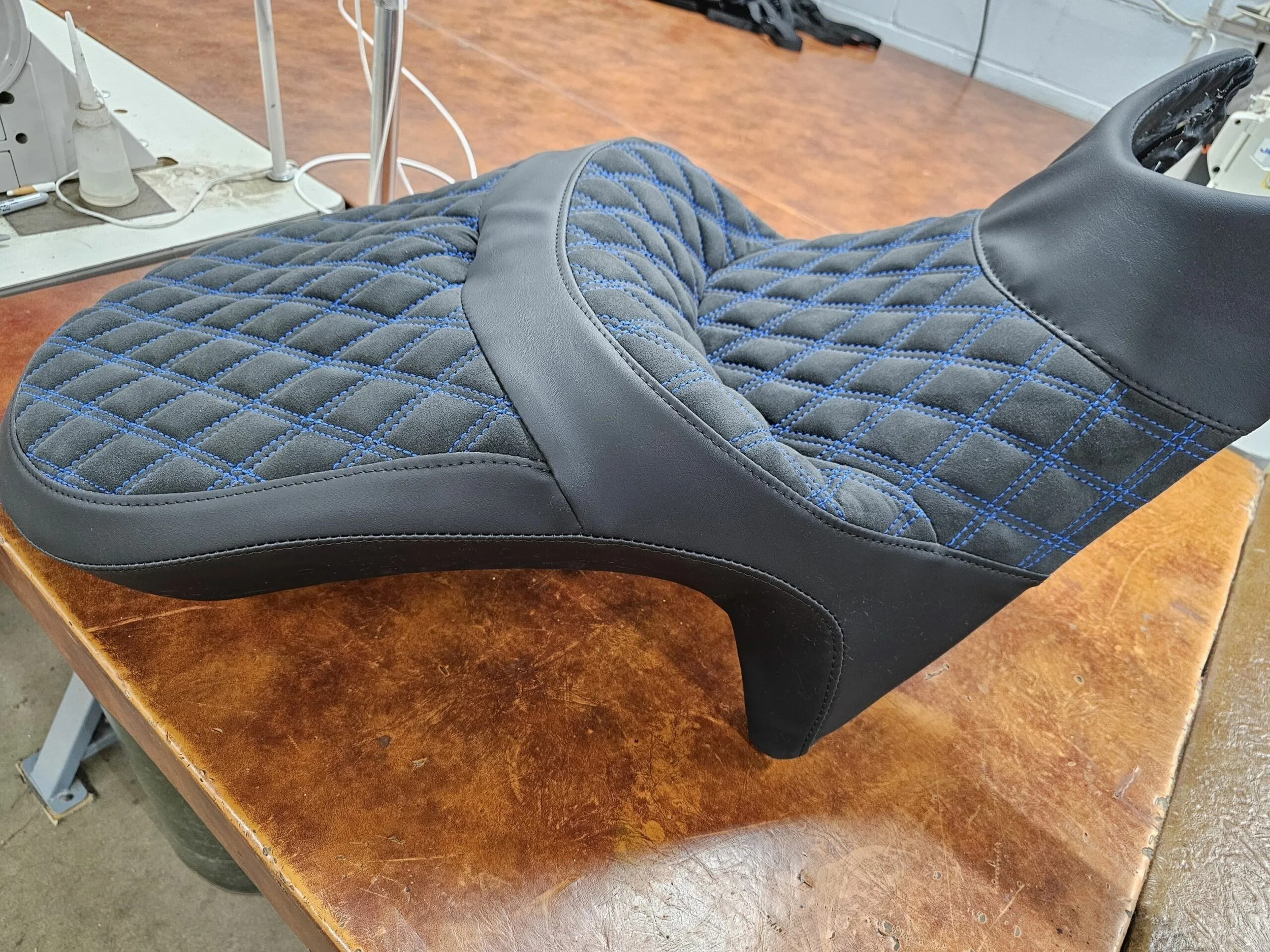 A black suede and vinyl motorcycle seat with blue diamond pleated stitching