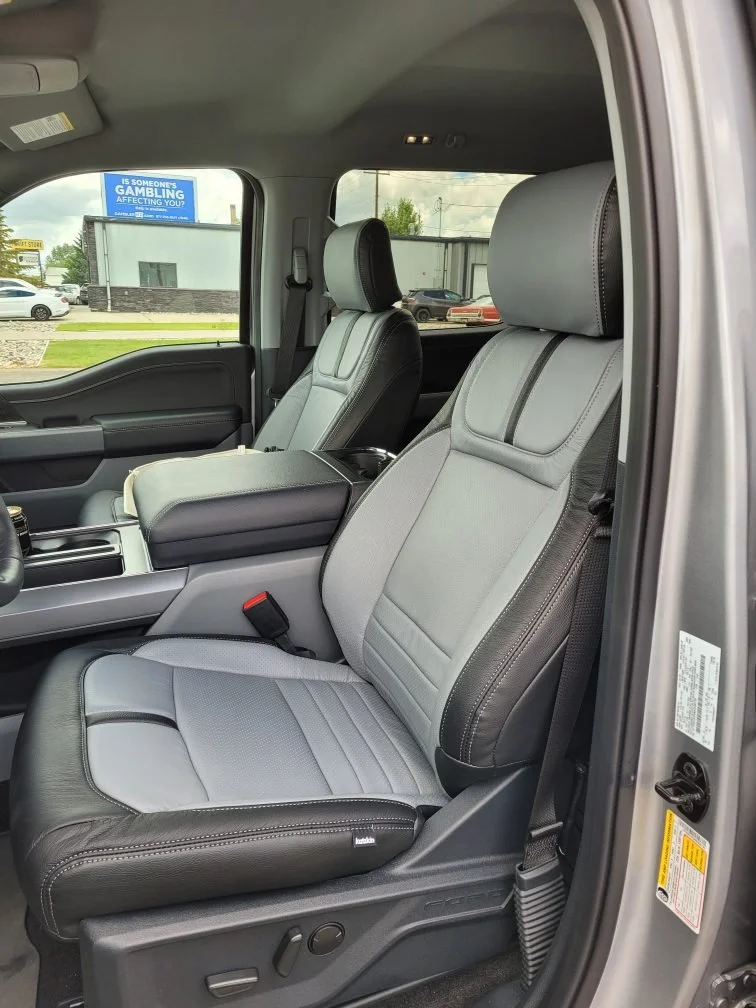 Inside view of a vehicle showing front driver and passenger seats with light gray (Lapis) upholstery and black accents. Katzkin Leather Kit.