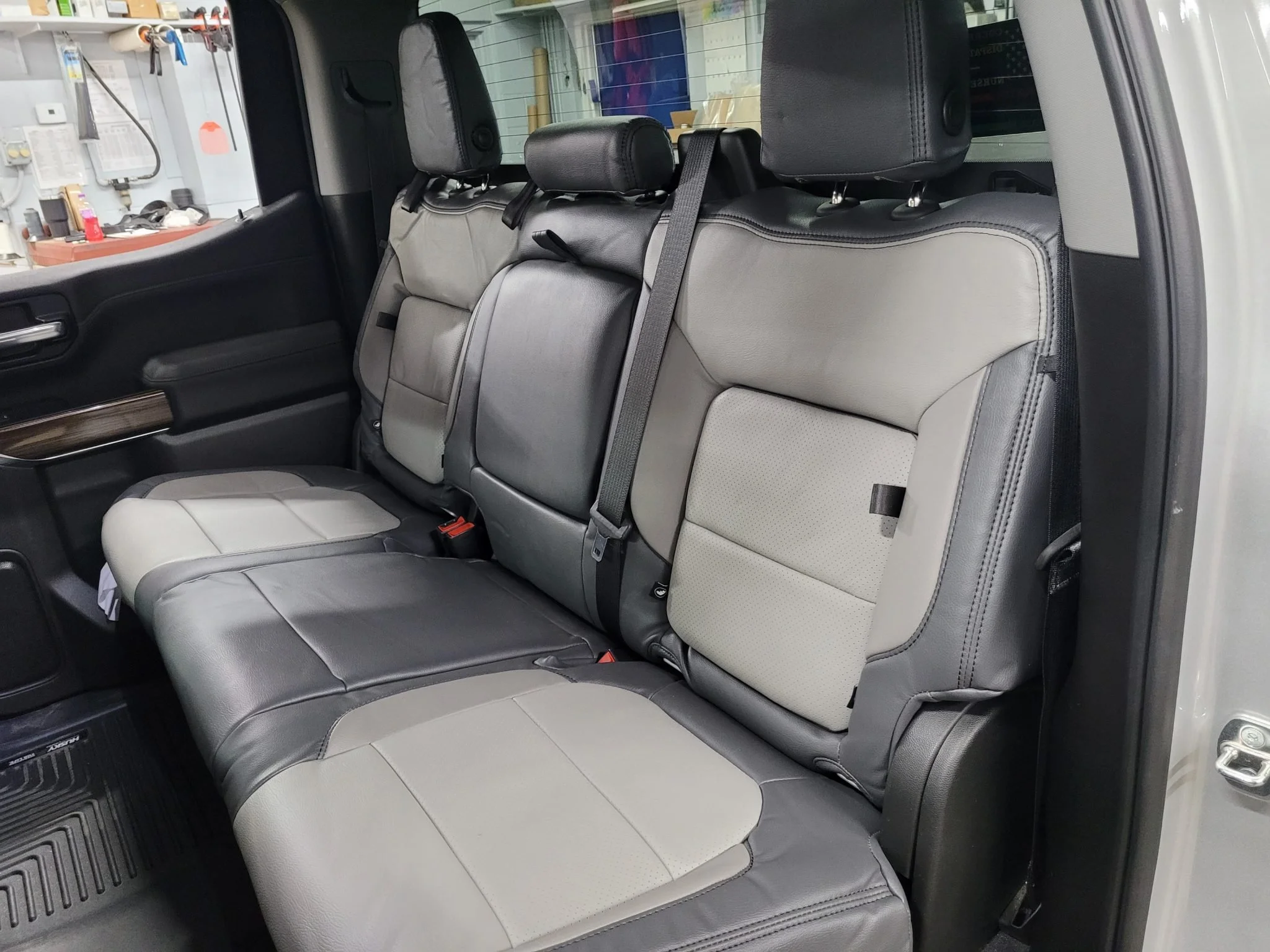 The back seat of a vehicle with leather upholstery, featuring a combination of light gray and darker gray seats, with three headrests. Katzkin Leather Kit.
