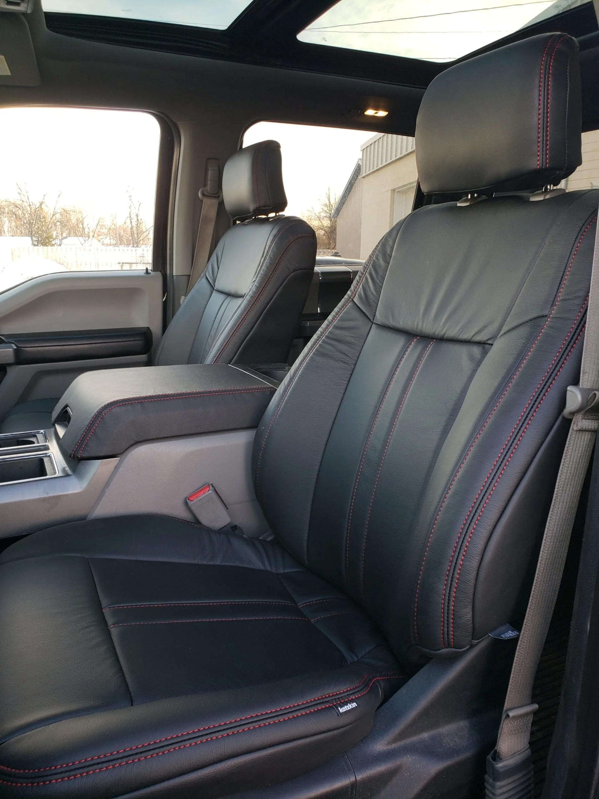 Inside a vehicle with front Katzkin leather seats featuring red stitching, black headrests, center console