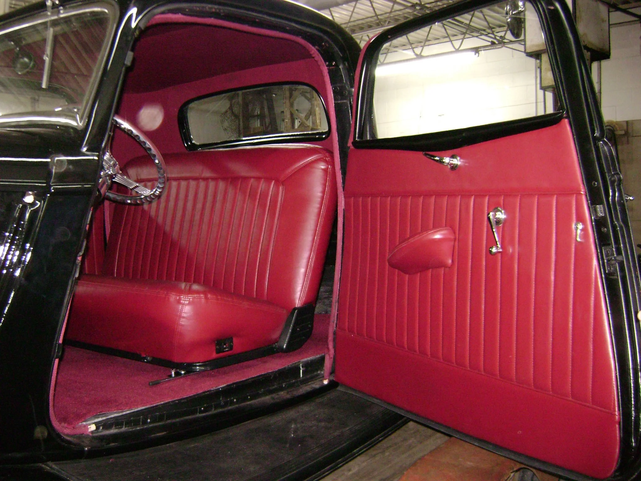 The interior of a vintage black and red car, showing red upholstered seats and door panels, with the door open.