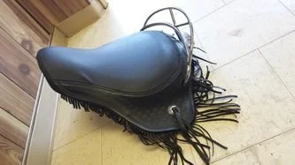 A black Western-style saddle with fringes on the sides
