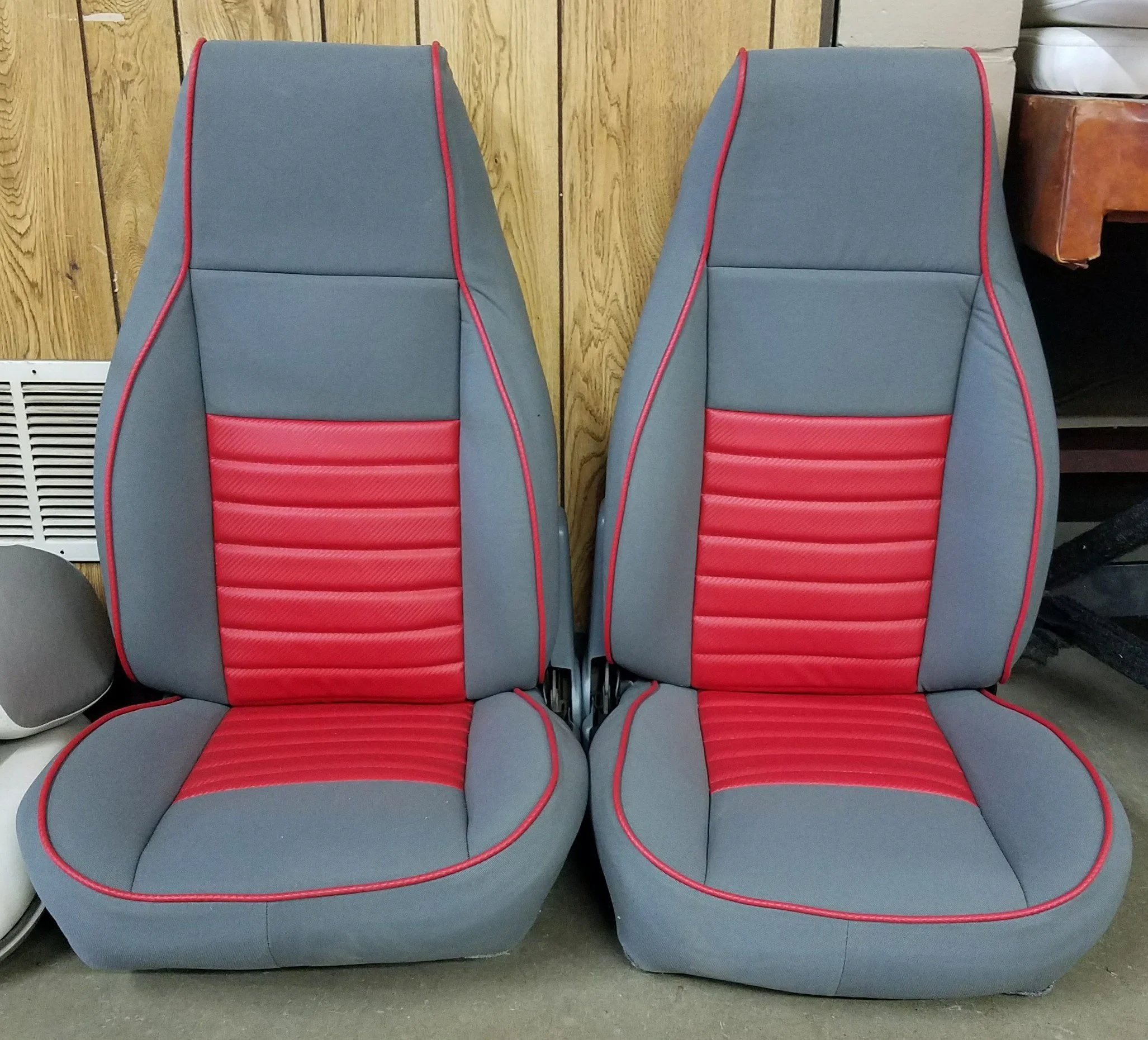 Two gray and red upholstered chairs with high backs and red piping, placed in front of a wooden wall.