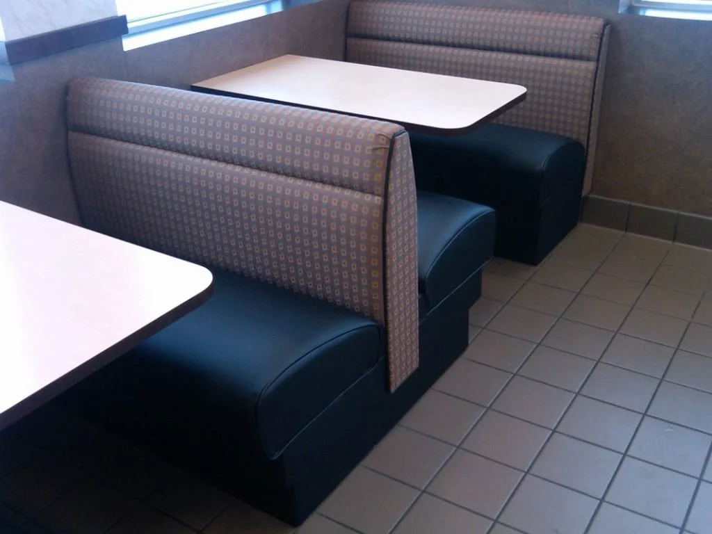 Booth seating in a restaurant with a table, patterned cushioned backrests, black vinyl seats.