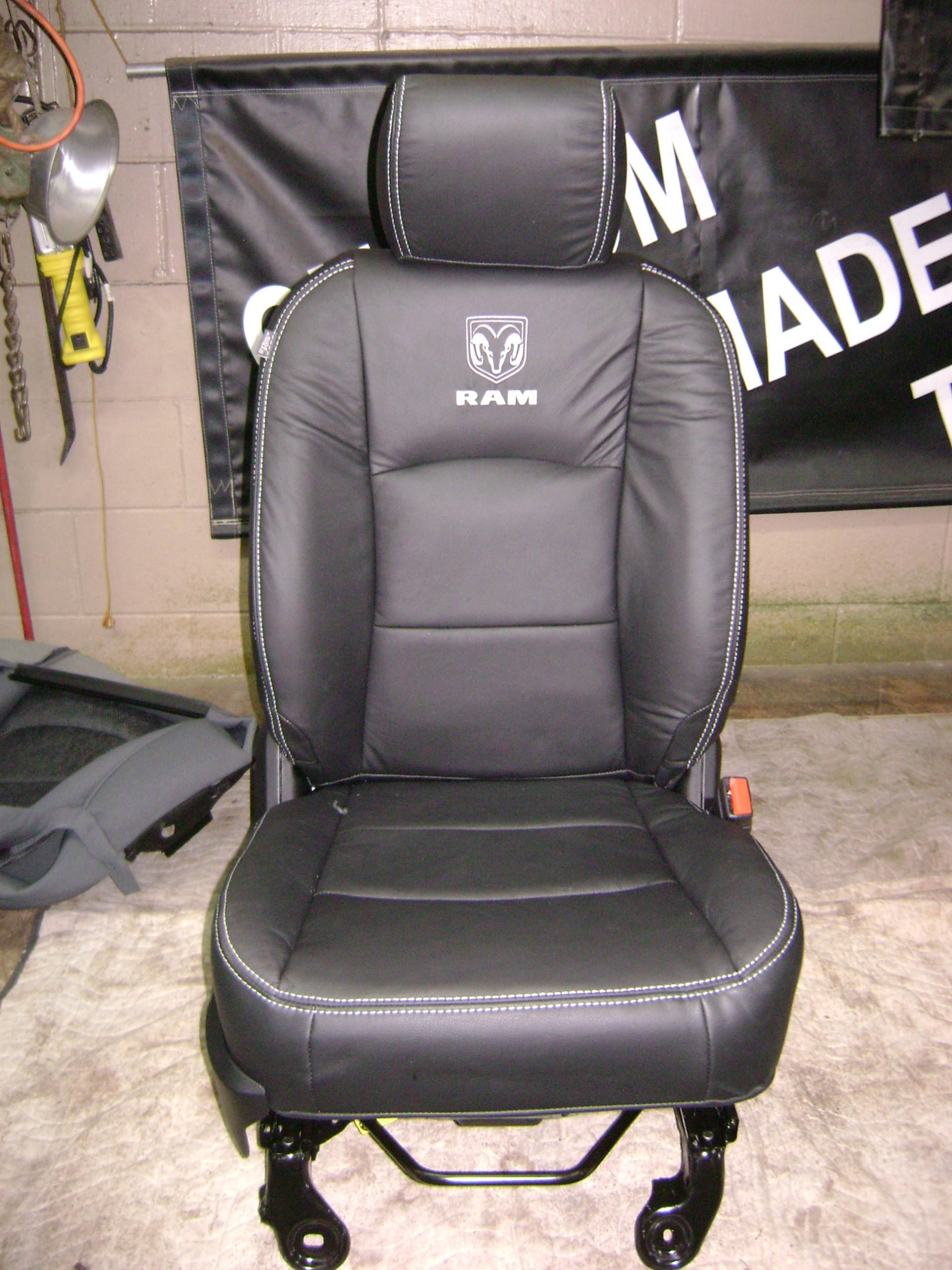 A black car seat with a headrest, featuring the RAM logo embroidered on the backrest of Katzkin Leather repalcment seat cover.