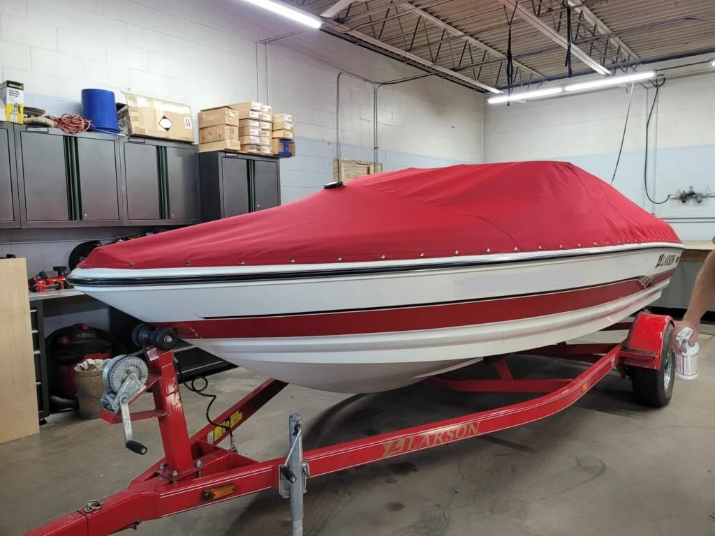 A boat covered with a red cover on a red trailer inside a workshop or garage.