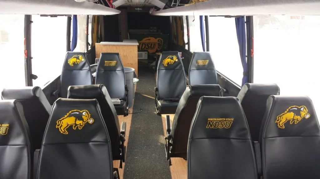Interior of a bus with black seats, each featuring a yellow and black North Dakota State University (NDSU) logo of a bison.
