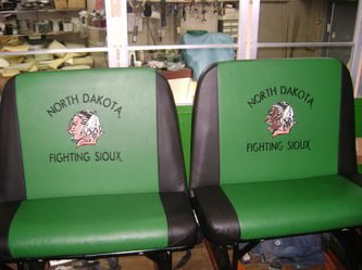 Two green bus seats with black accents, featuring images of a Sioux warrior and the words 'North Dakota Fighting Sioux' on the backrests.