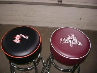 Two round padded seats, one black with red trim and the other maroon, with school logos