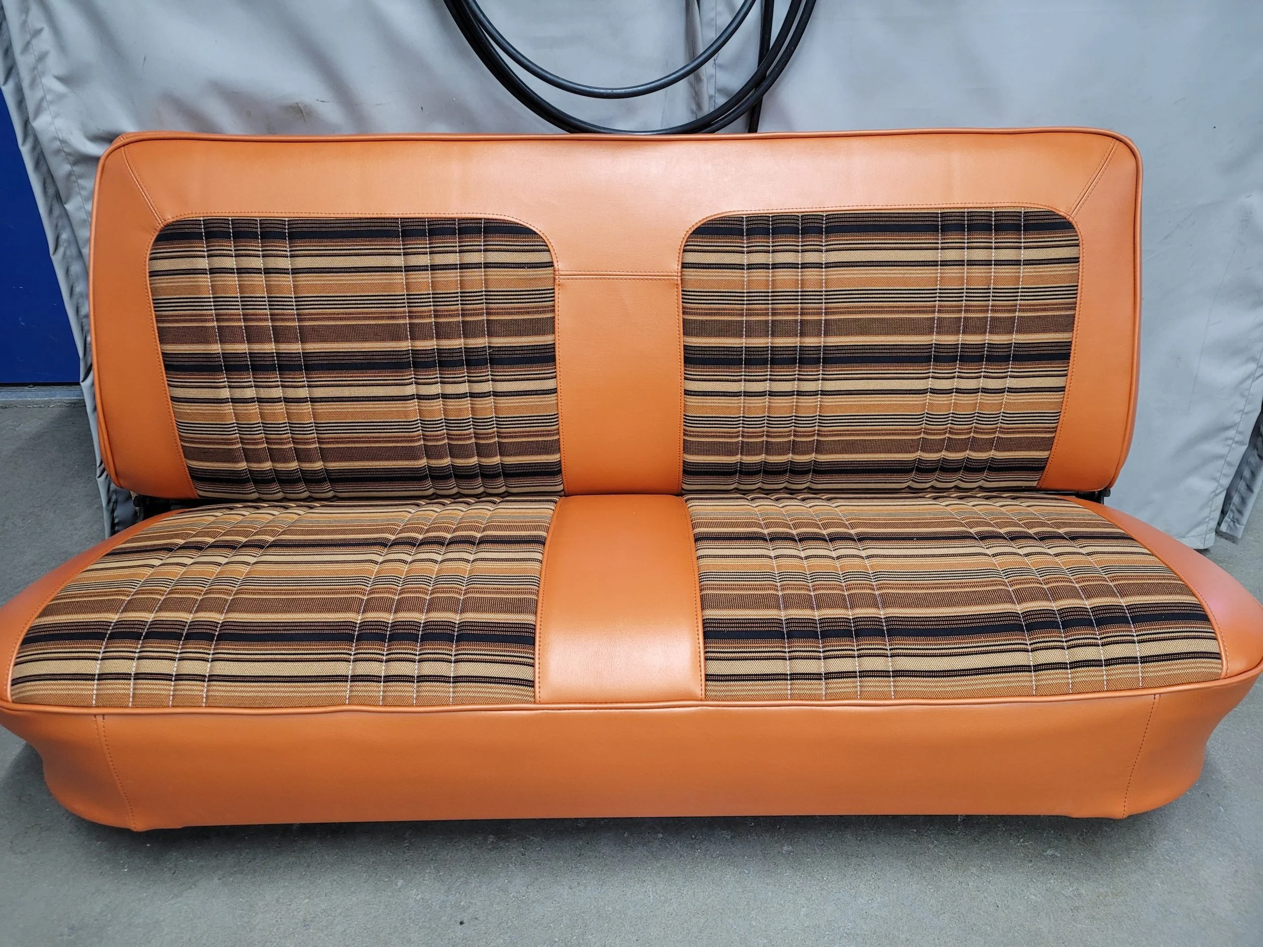 A vintage style orange upholstered car bench with plaid patterned fabric in the center sections, known as "Orange Crush"