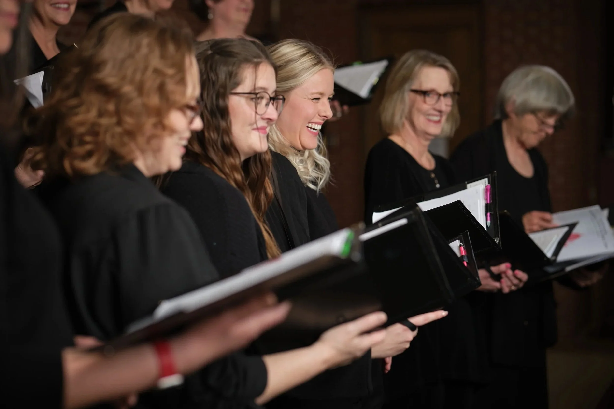 Members of Good Company, Ames Women's Choir singing during a choir concert, holding black folders with sheet music.