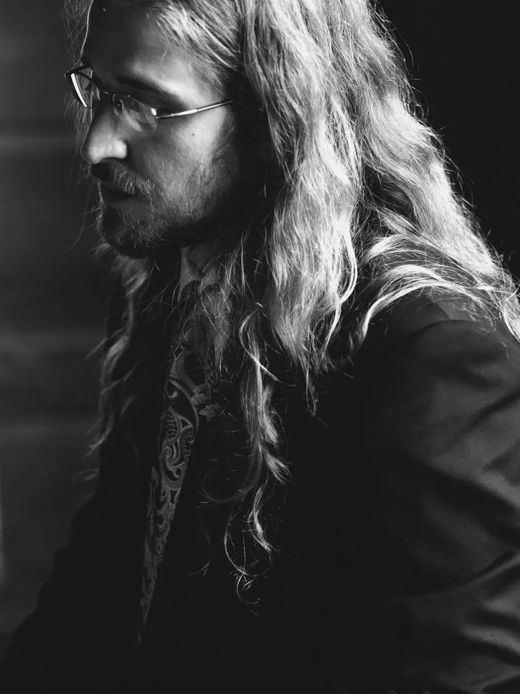 Black and white photo of collaborative pianist with Good Company, Peter Roberts, with long, wavy hair and glasses, looking down.