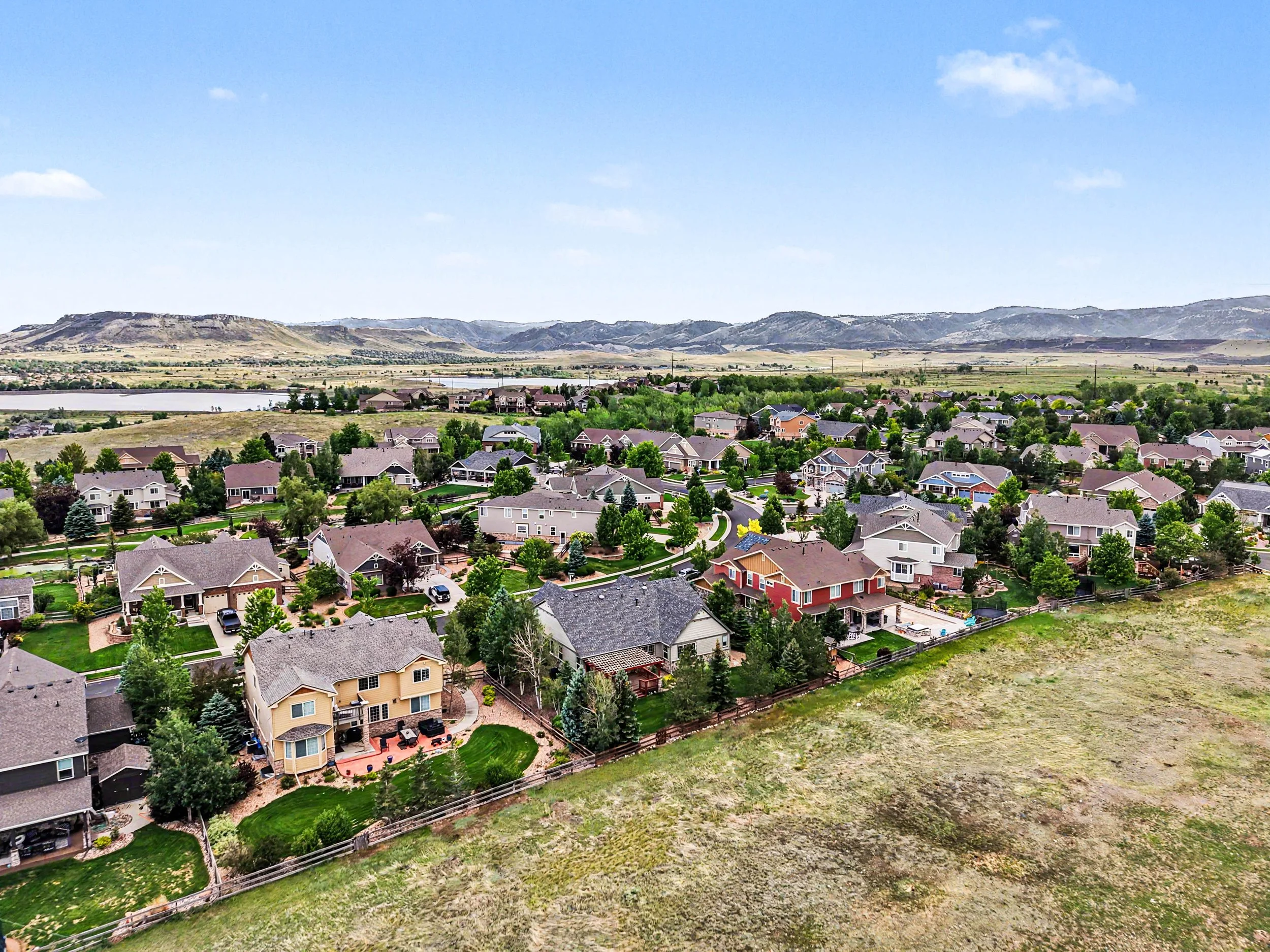 A suburban neighborhood with houses and lush greenery, set against a background of rolling hills under a bright blue sky with scattered clouds.