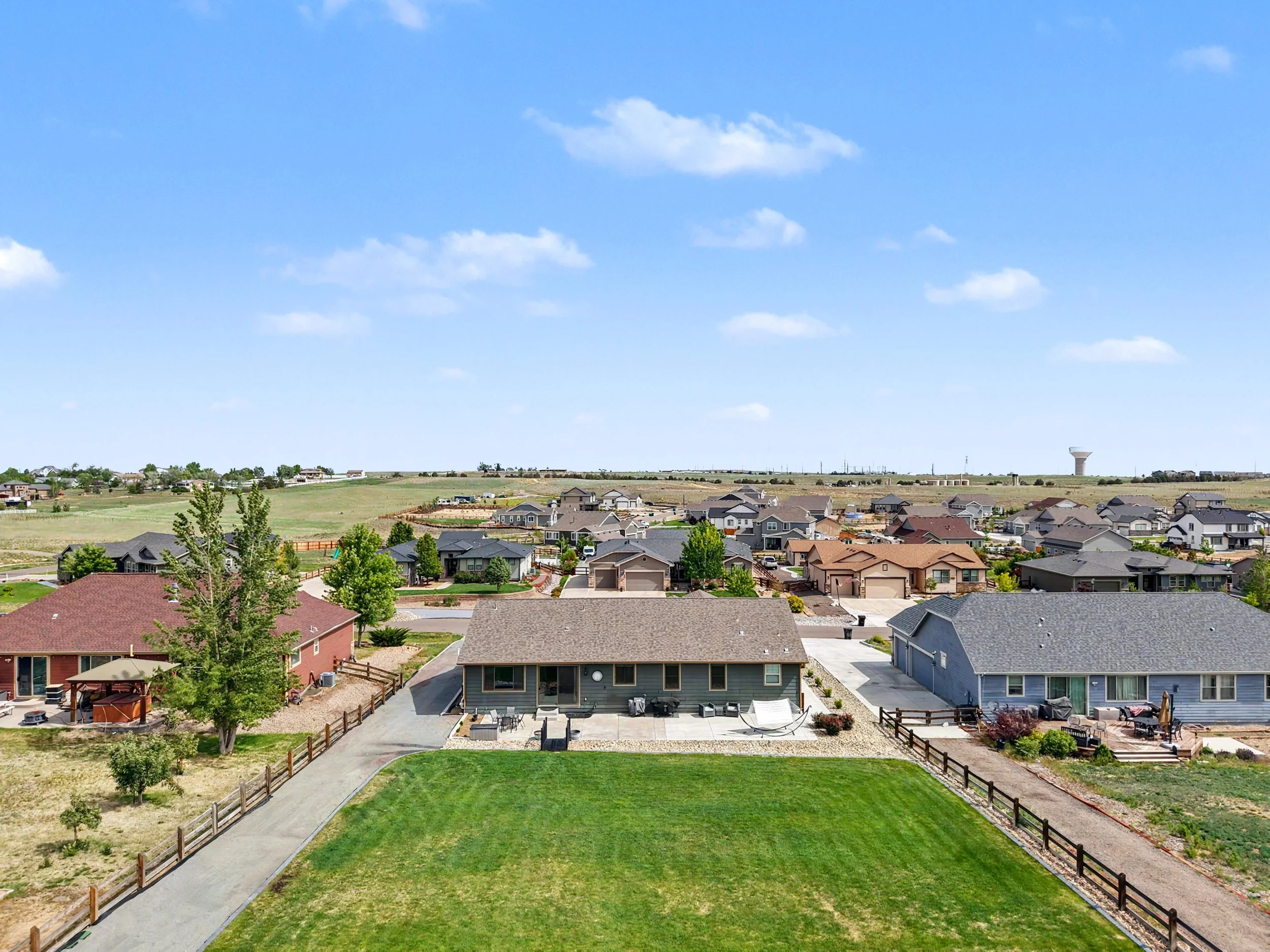 A suburban neighborhood with houses, green lawns, and trees under a blue sky with scattered clouds.