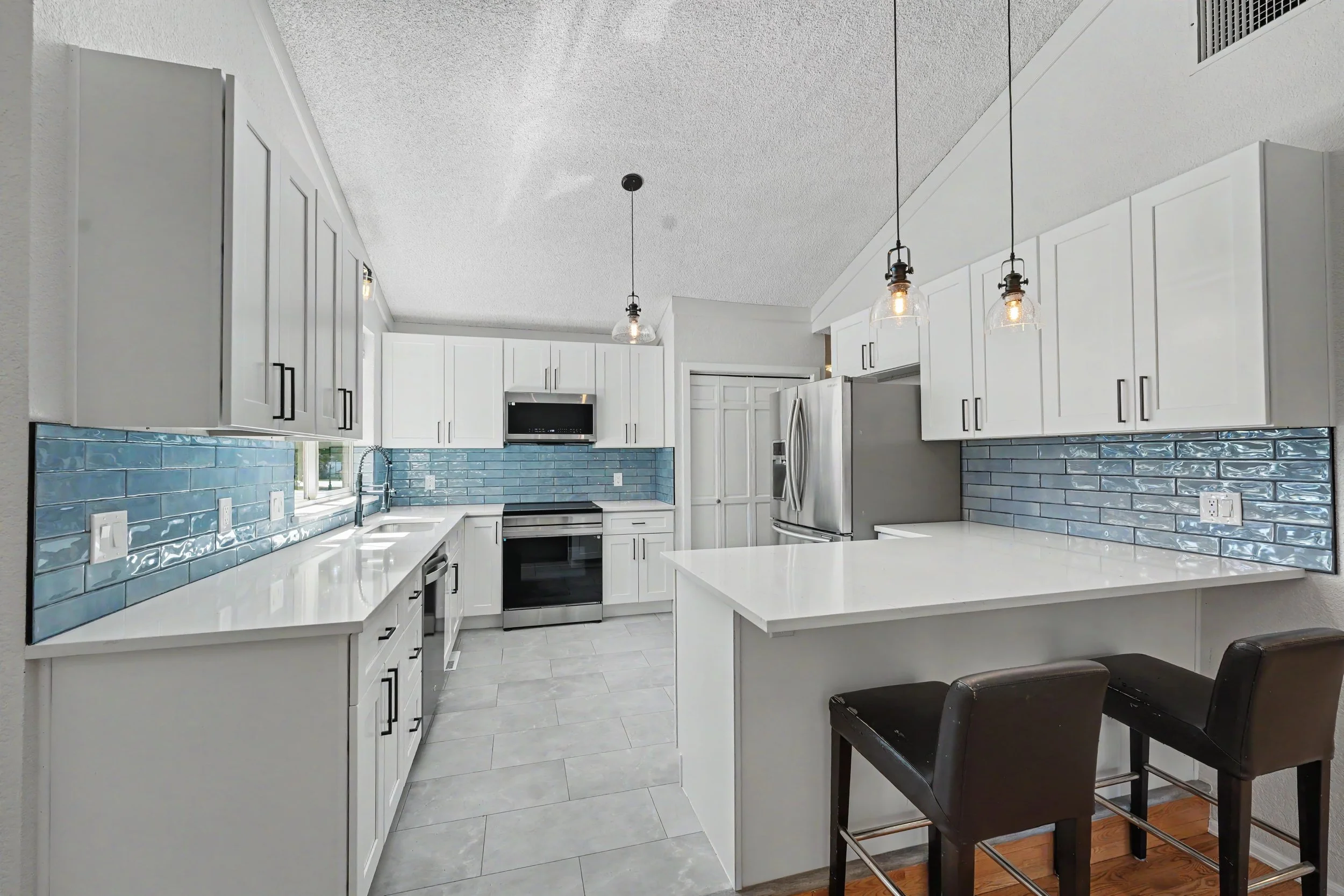 Modern kitchen with white cabinets, blue subway tile backsplash, stainless steel appliances, and black barstools at a white countertop