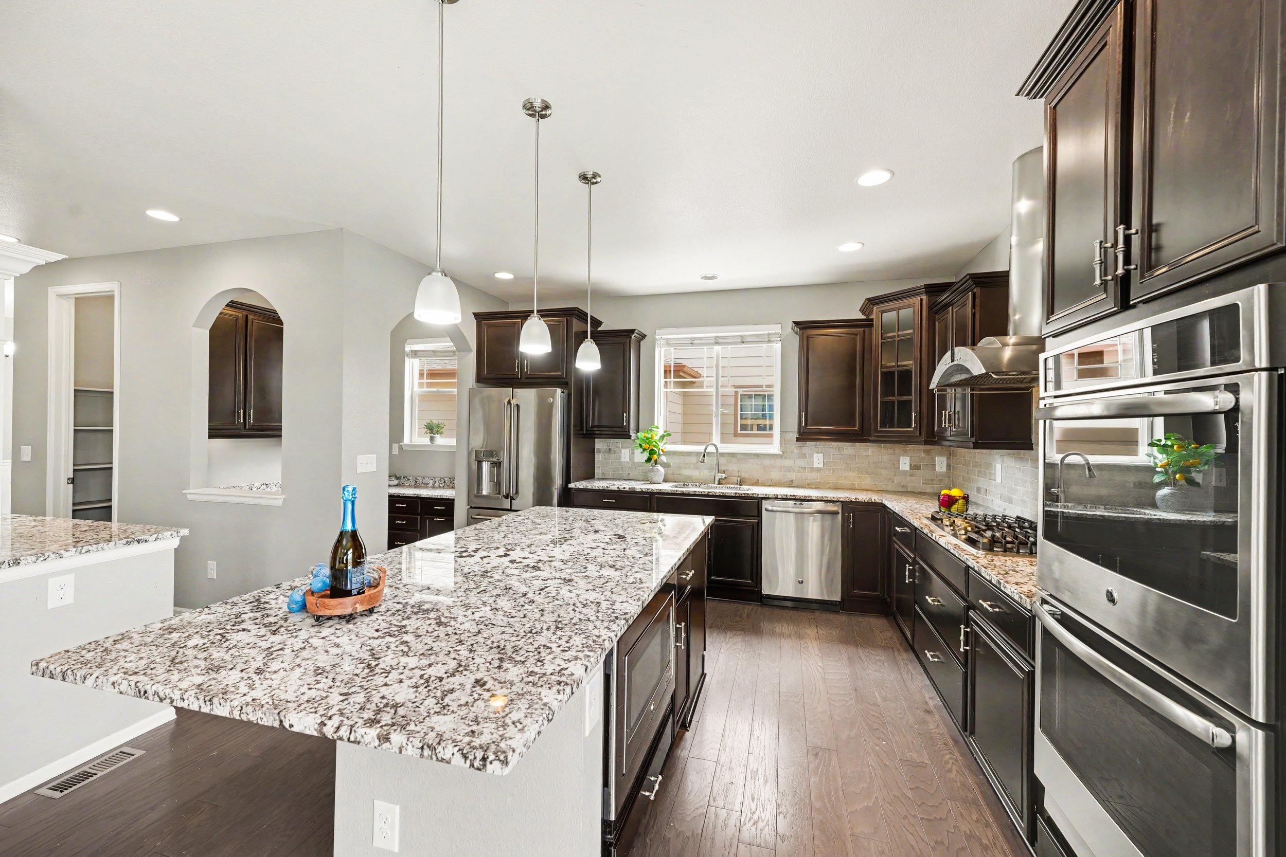 Modern kitchen with granite countertops, dark wood cabinets, stainless steel appliances, pendant lighting, and a window with white blinds.