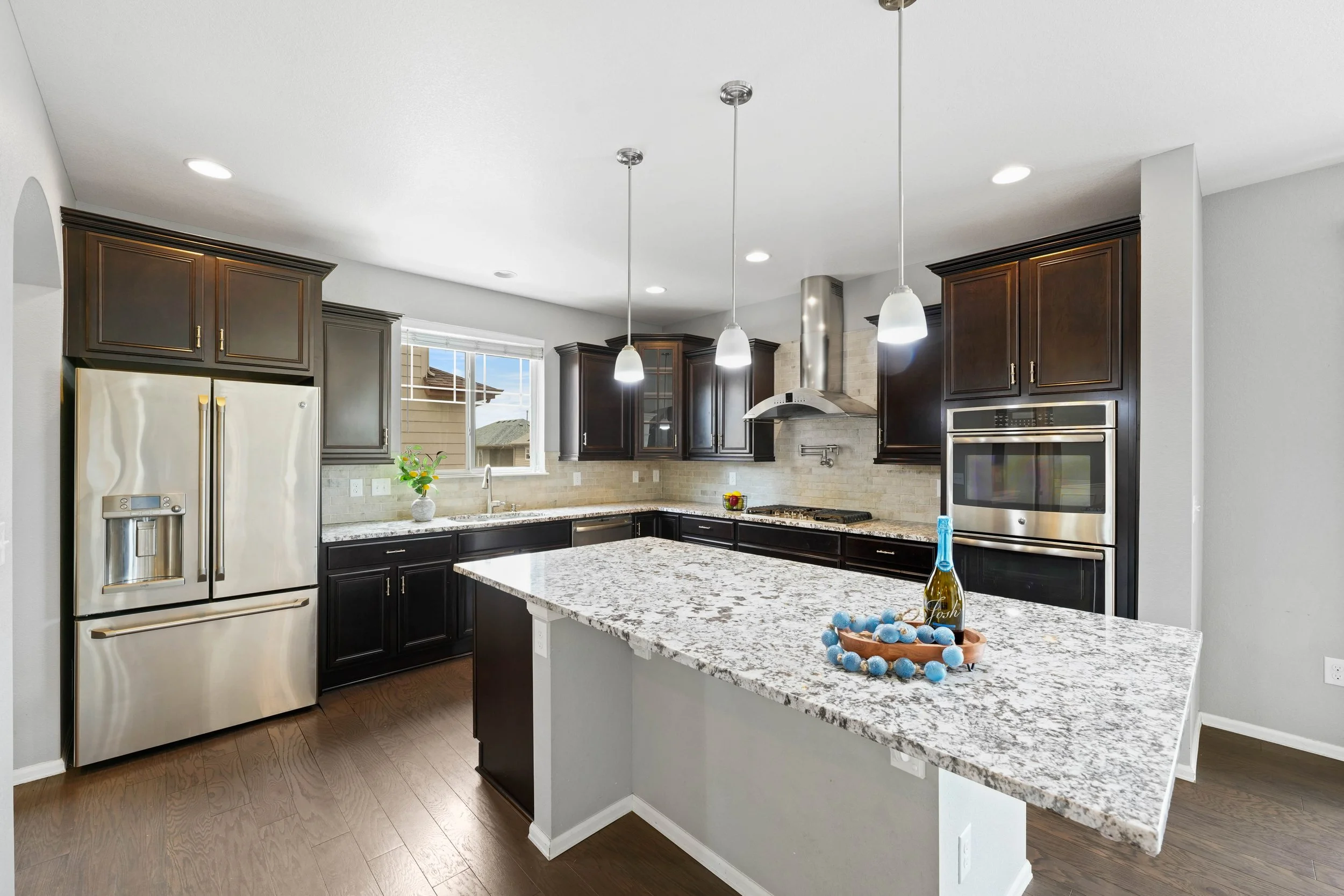 Modern kitchen with dark wood cabinets, stainless steel appliances, a granite island, and pendant lighting.