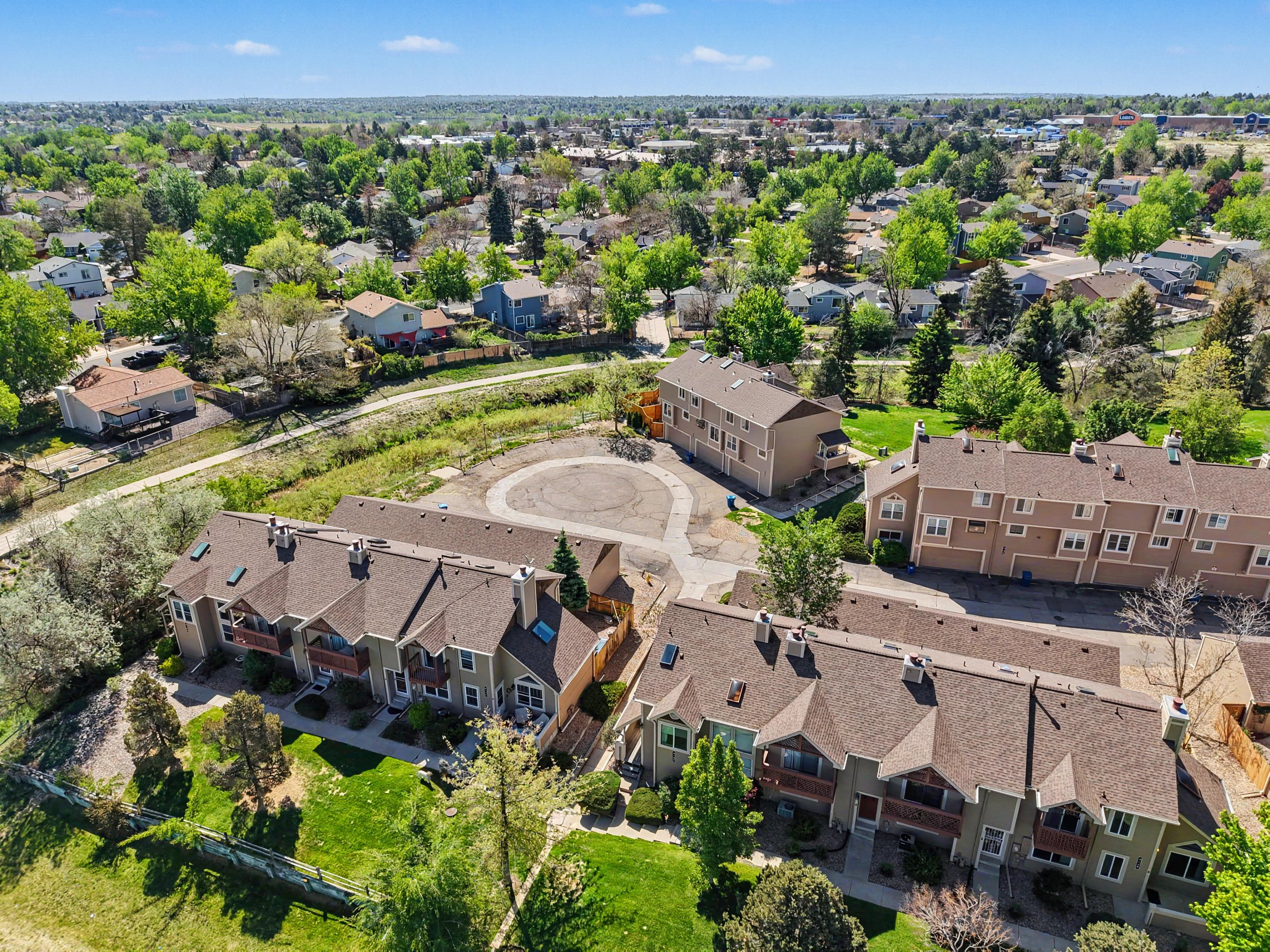 Aerial view of a suburban neighborhood with numerous houses, green trees, and a clear blue sky.