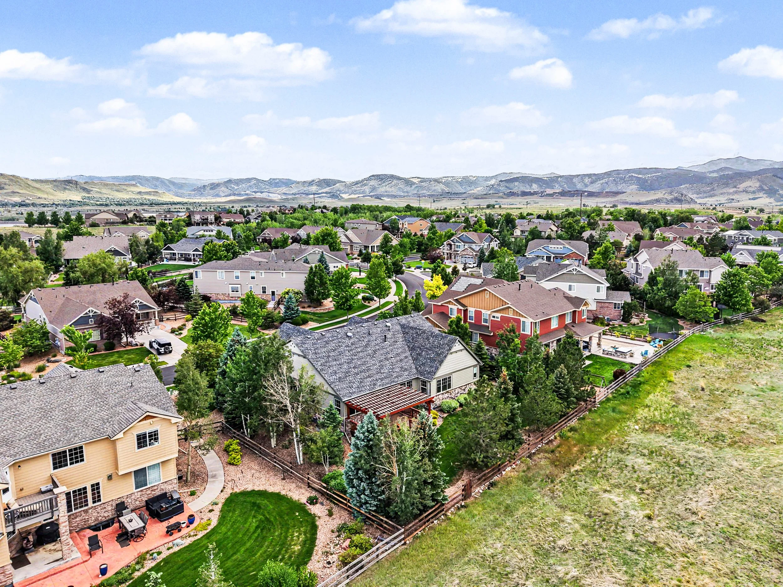 A suburban neighborhood with houses, green trees, and a yard, with mountains in the background and a partly cloudy sky.