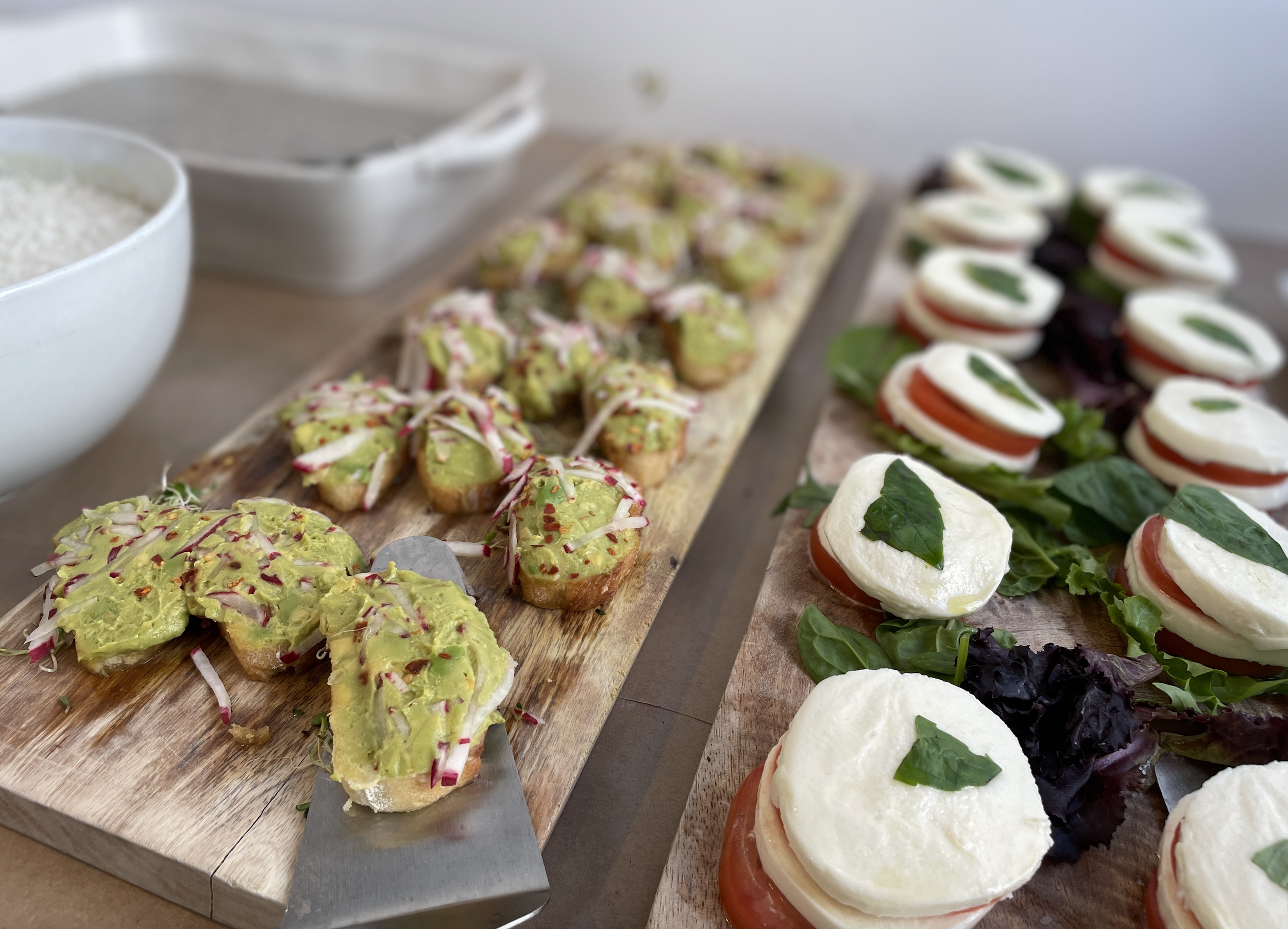 Assorted appetizers on wooden serving boards, including sliced mozzarella, tomatoes, basil, and cheese, along with colorful topped bruschetta or crostini with toppings like avocado and pink drizzle.