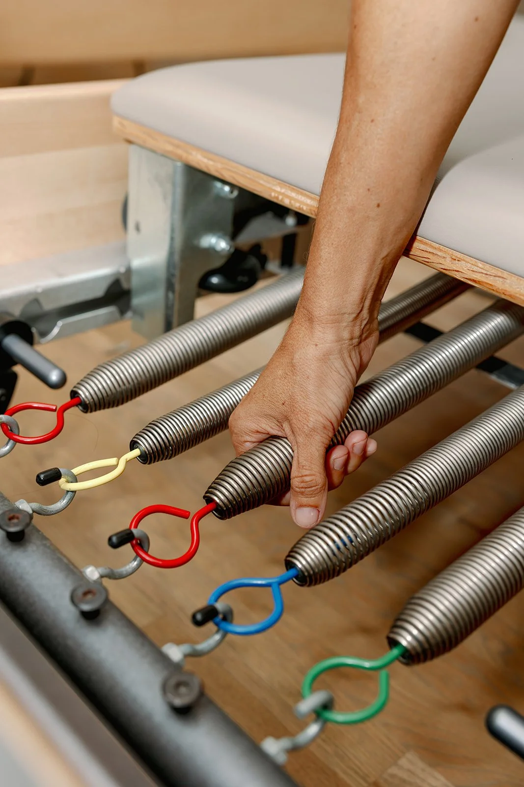 Close-up of a person's hand gripping a metal spring connected to wires on a wooden and metal structure.