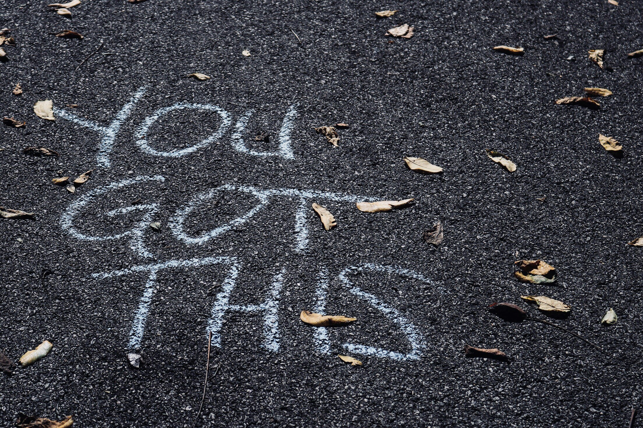 A sidewalk with chalk drawing of the year '2023' and scattered dry leaves.