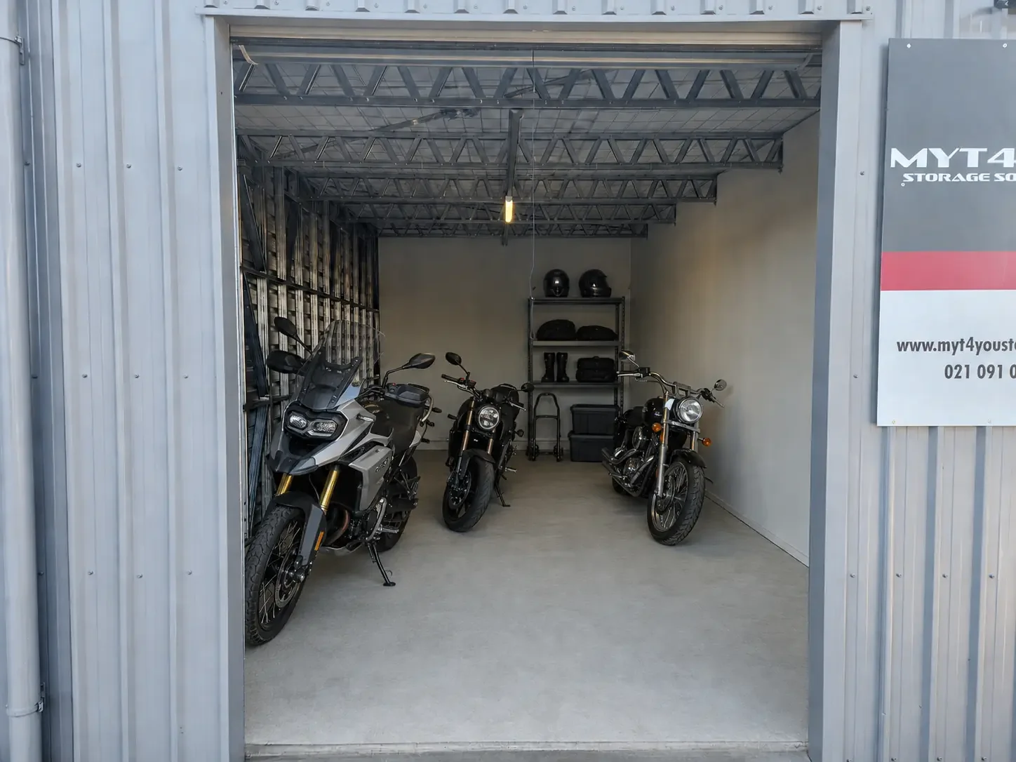 Three motorbikes and riding equipment stored inside a drive-up unit at Myt4you Storage Ravenswood
