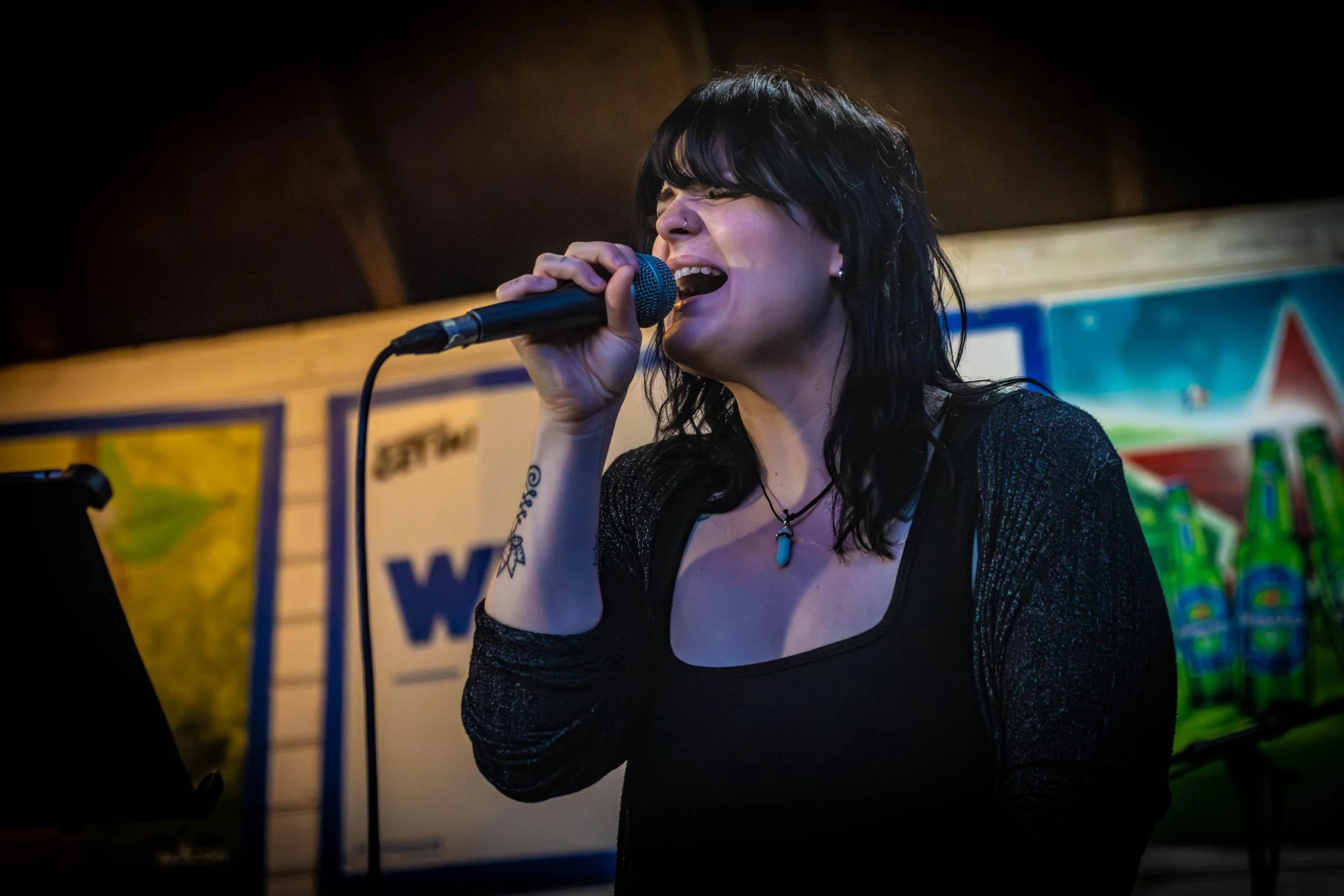 A woman singing into a microphone on stage, with a colorful banner in the background.