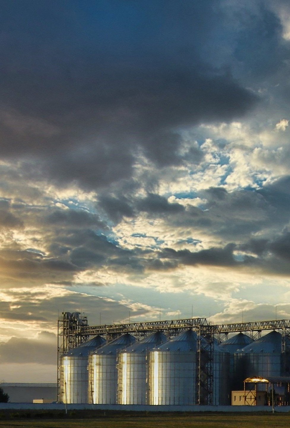 Industrial storage silos under cloudy sky at sunset.