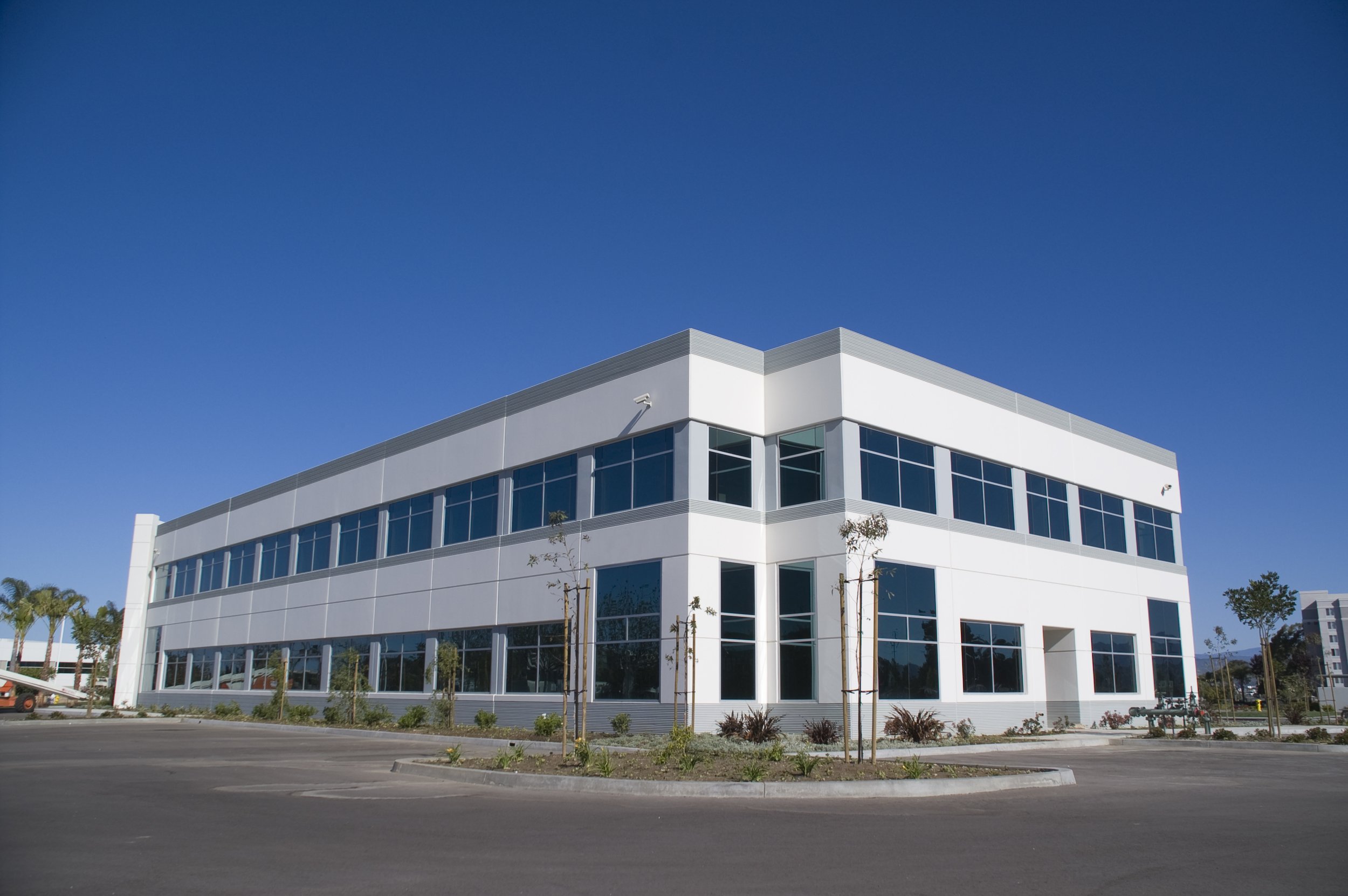 Modern white commercial building with large glass windows under a clear blue sky.