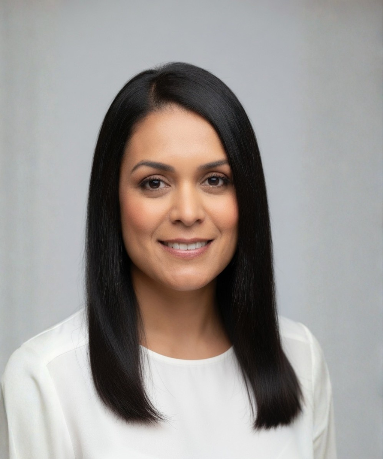 A professional woman with straight black hair, light makeup, and a smile, wearing a white top, standing against a plain gray background.