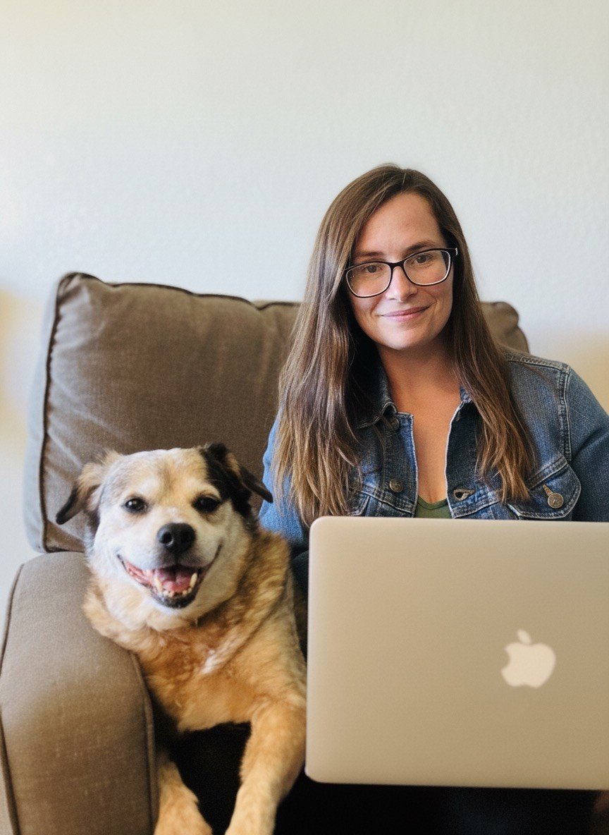 Photo of Virginia Gearhart, Founder of Gearhart Bookkeeping | A woman with long brown hair, glasses, and a denim jacket sitting on a sofa with a smiling dog next to her, laptop open in front of them.