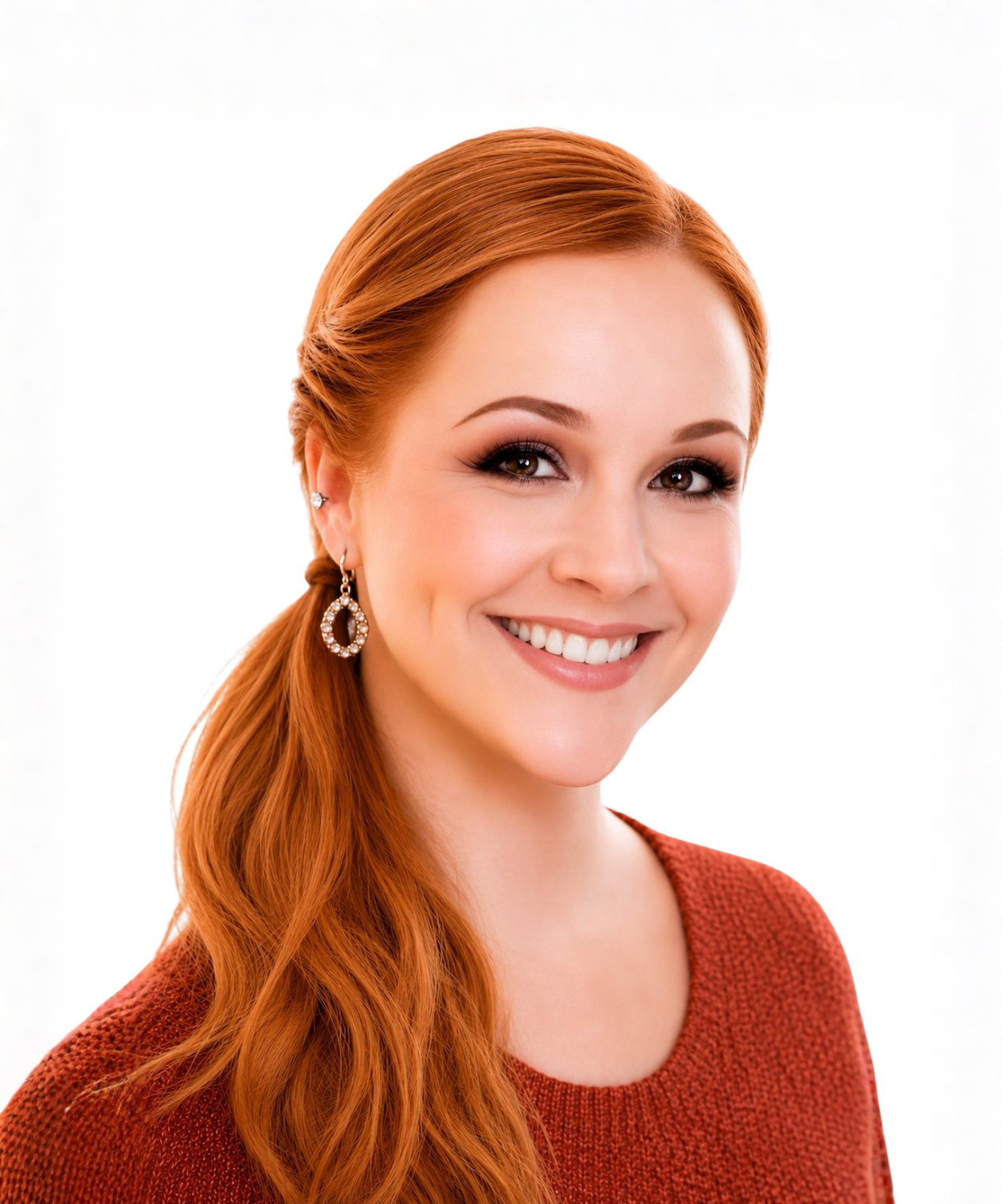 Portrait of a young woman with long red hair, smiling, wearing earrings and a red sweater, against a white background.