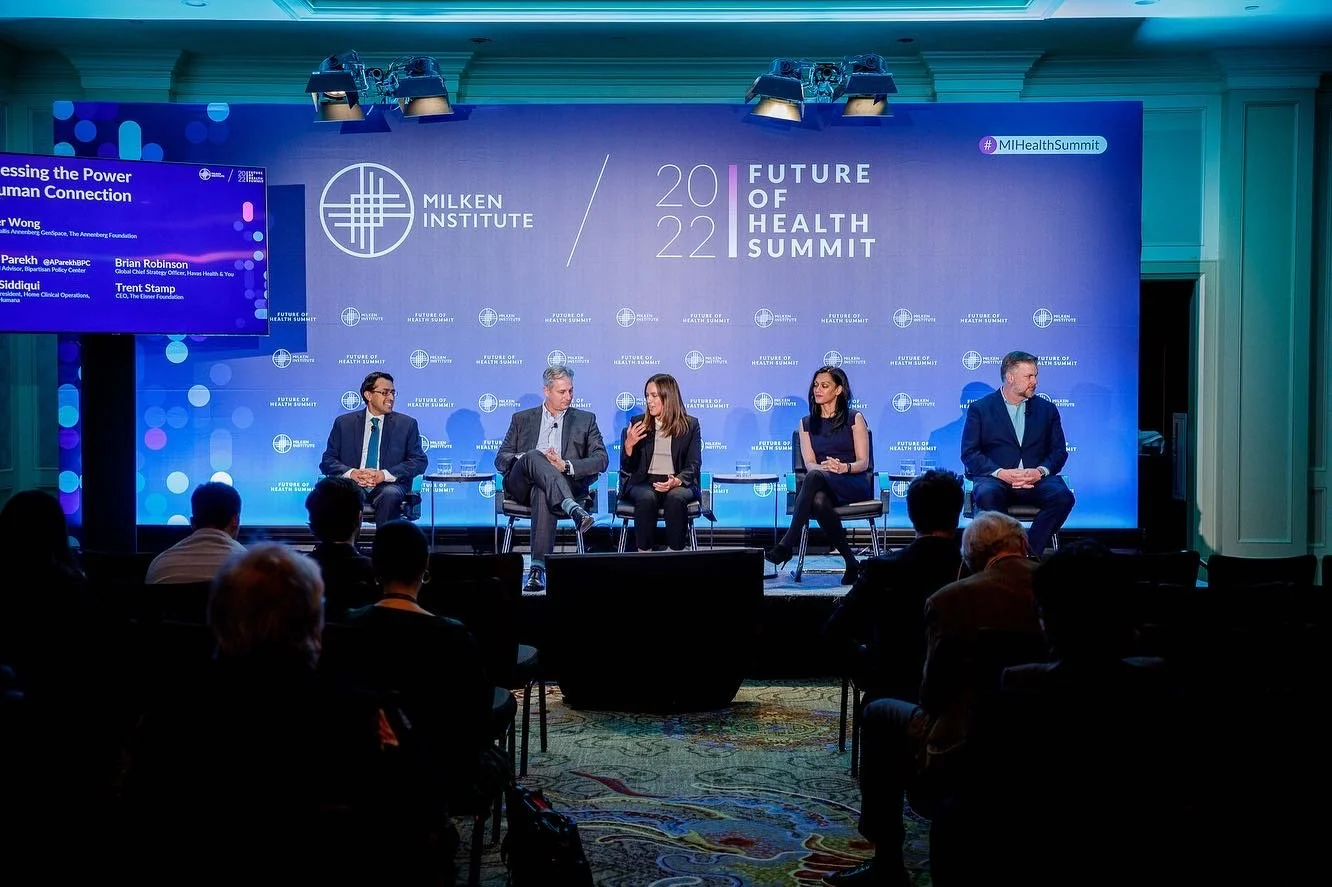 Panel discussion at the 2022 Future of Health Summit hosted by the Milken Institute, featuring five speakers on stage, with a large blue backdrop and audience in the foreground.