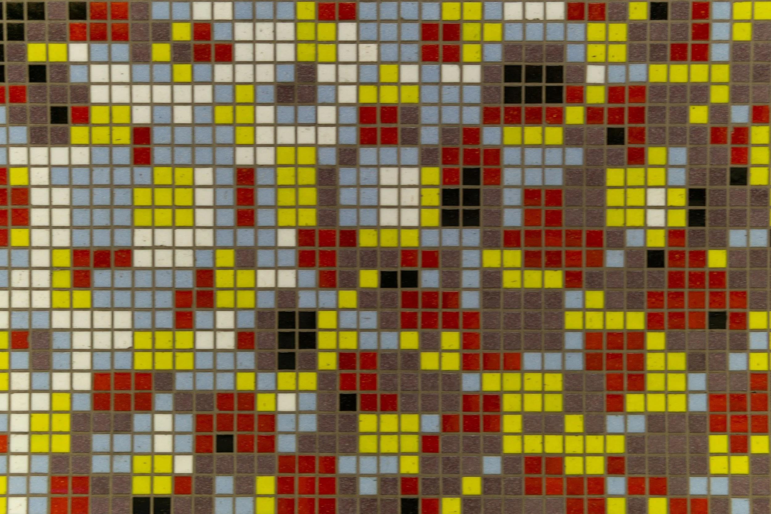 Close-up of a mosaic tile wall with small square tiles in yellow, red, white, black, and light blue colors.
