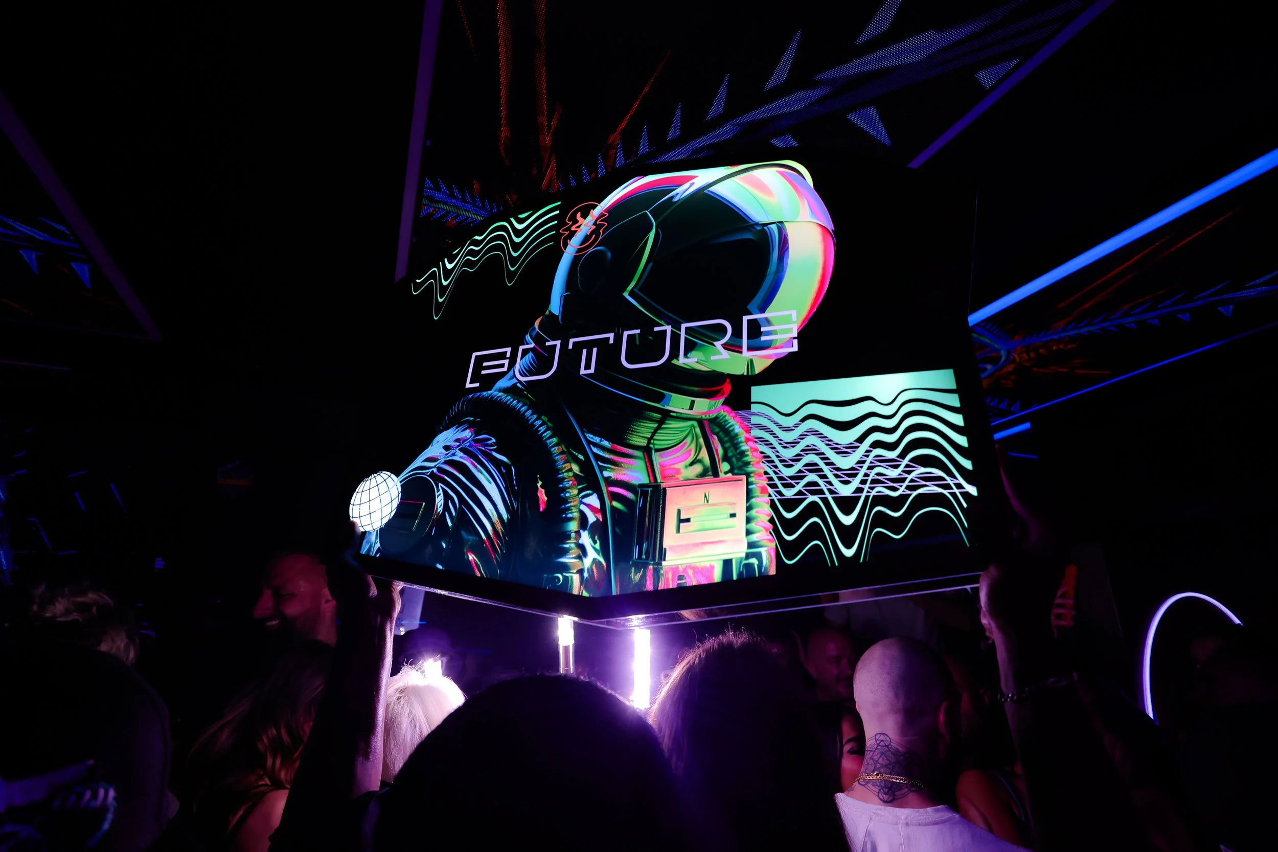 Crowd at a dark event with a large digital display showing an astronaut helmet with the word 'FUTURE' and neon light effects.
