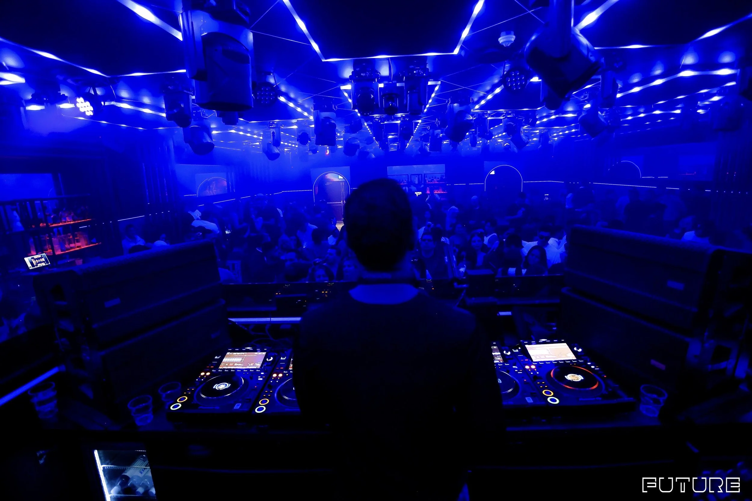 A DJ playing music in a nightclub with blue neon lighting and a large crowd of people dancing.