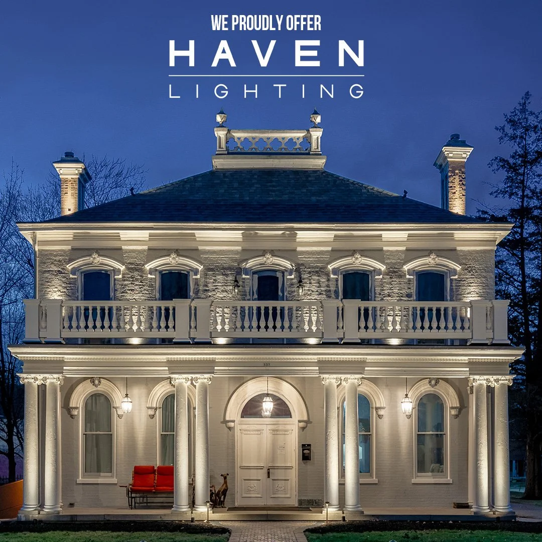 A large, historic, white house illuminated at night, showcasing decorative columns, arched windows, and balconies. Text overlay states, 'We proudly offer Haven Lighting.'